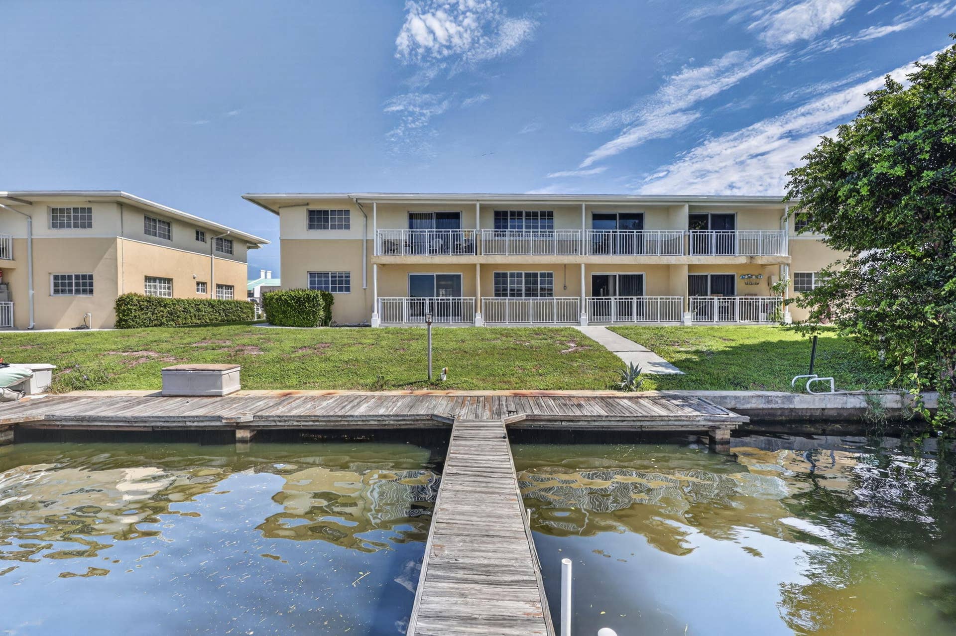 405 SOUTHWIND Drive, #3, North Palm Beach, FL 33408 Multi-level waterfront building featuring wooden boat dock, private balconies with metal railings, sliding glass doors, and expansive lawn area