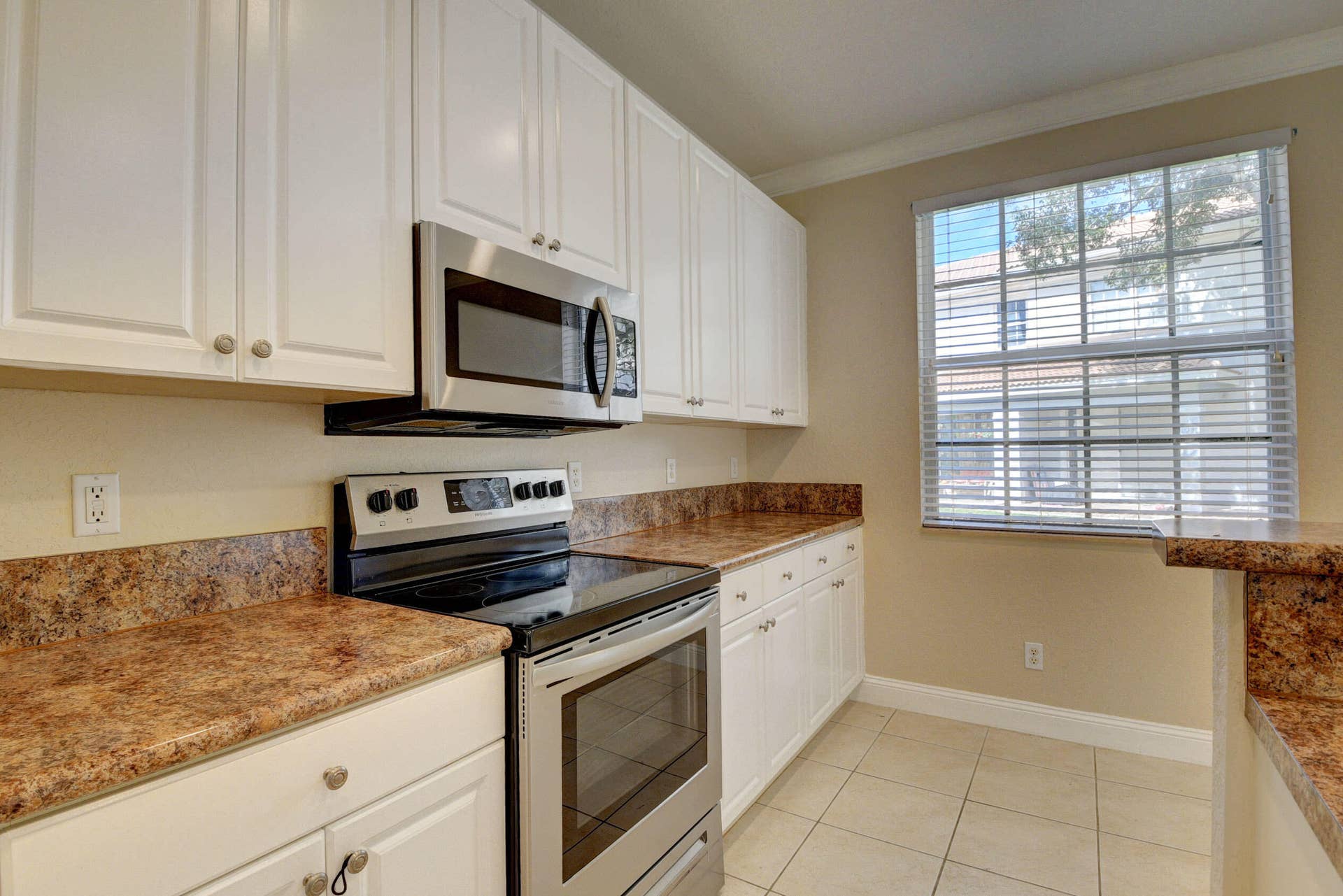 4353 Legacy Court, Delray Beach, FL 33445 Stainless steel range and over-the-range microwave with white cabinets and a bright window.