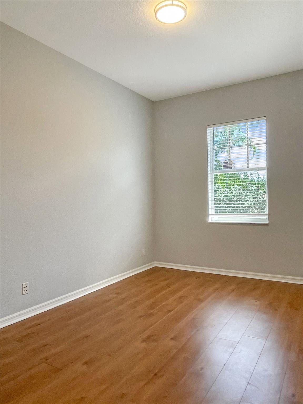 5780 NW 120TH Avenue, Coral Springs, Coral Springs, FL 33076 Room featuring wood-finish flooring, neutral wall paint, and a singular window with horizontal blinds, illuminated by a flush-mount ceiling fixture