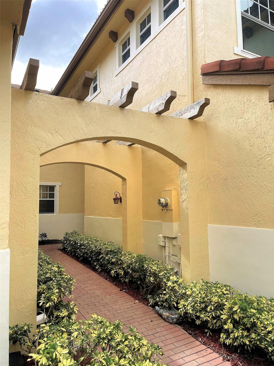 5780 NW 120TH Avenue, Coral Springs, Coral Springs, FL 33076 Stucco exterior featuring dual arched walkways, exposed timber rafters, and a brick-paved path bordered by mature shrubbery