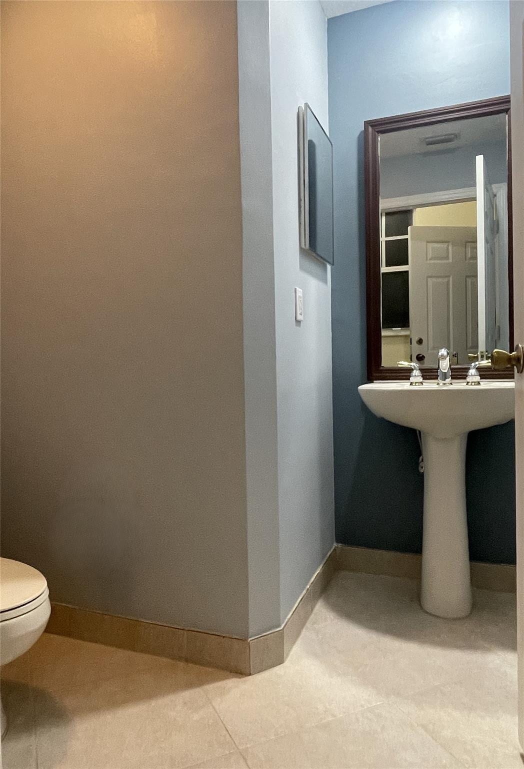 5780 NW 120TH Avenue, Coral Springs, Coral Springs, FL 33076 Pedestal sink featuring a polished chrome faucet, wall-mounted dark wood-frame mirror, and neutral-tone tile flooring