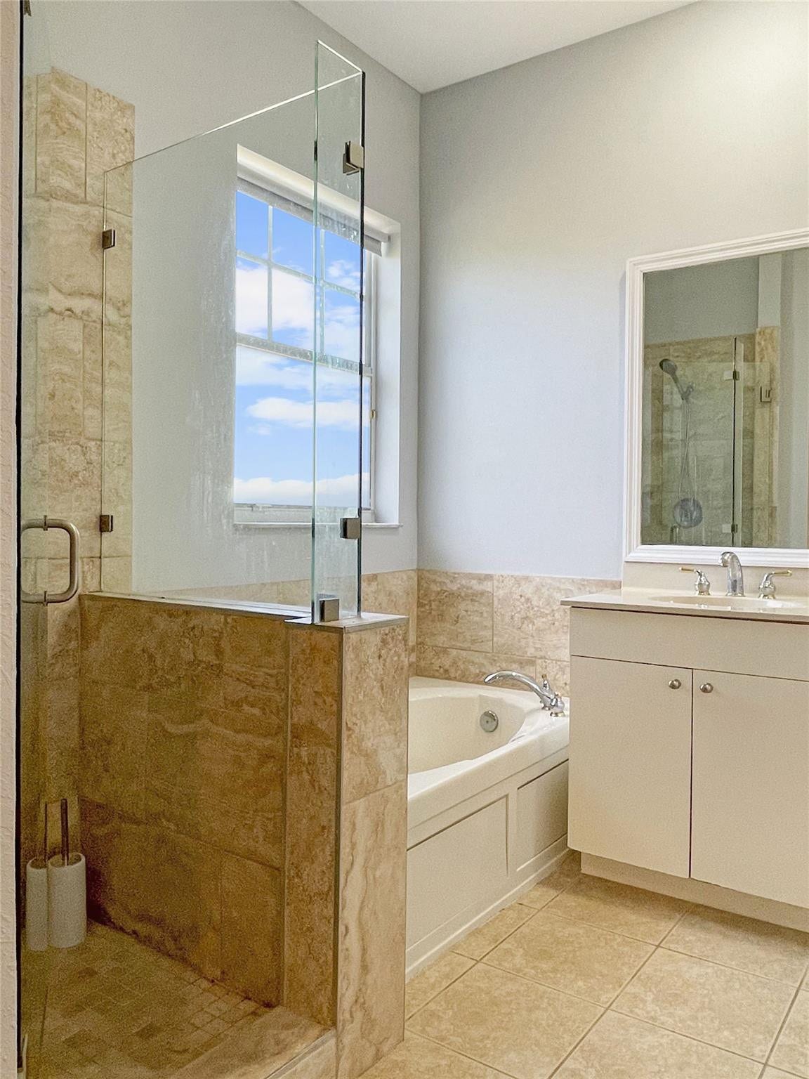 5780 NW 120TH Avenue, Coral Springs, Coral Springs, FL 33076 Bathroom featuring a glass-enclosed shower with stone-finish wall tile, a deep soaking tub, and a white vanity with a polished metal faucet