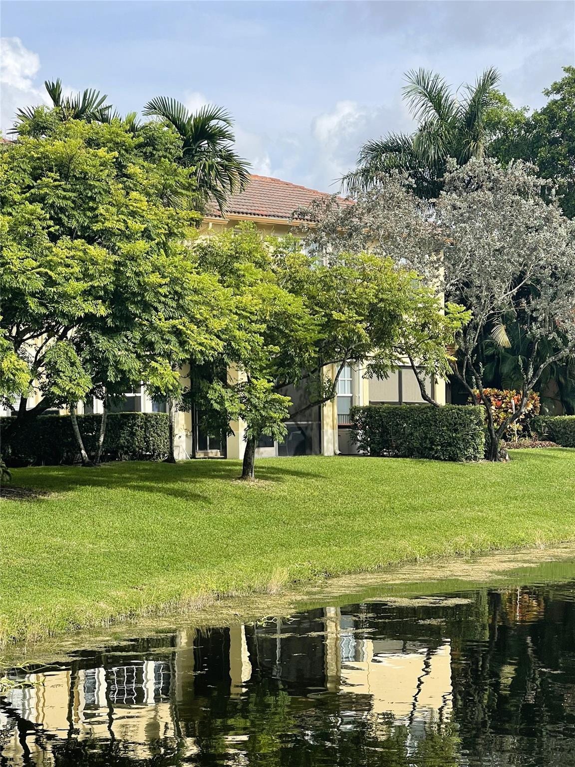 5780 NW 120TH Avenue, Coral Springs, Coral Springs, FL 33076 Waterfront property featuring a tiled roof, screened-in exterior space, and mature perimeter landscaping