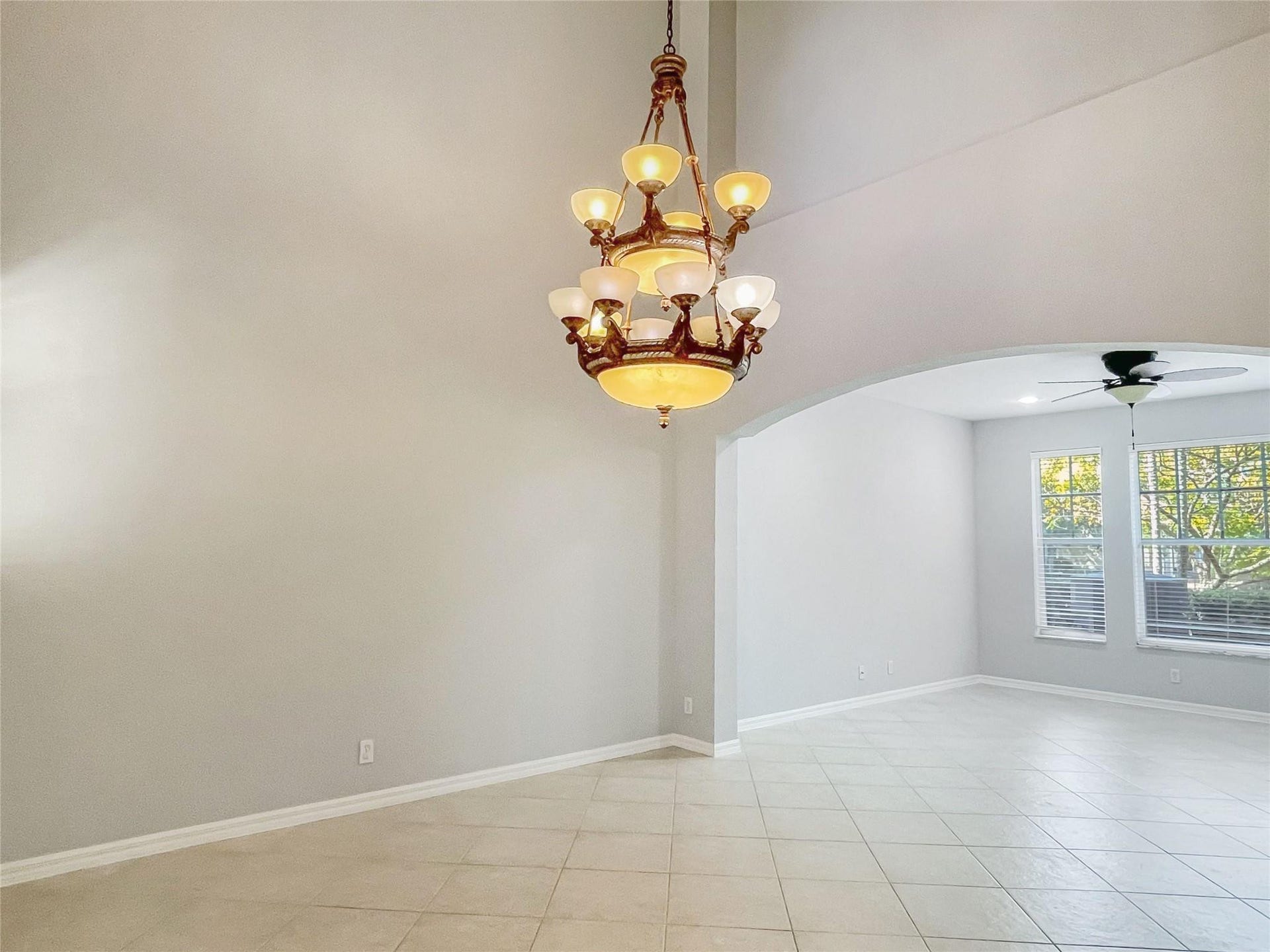 5780 NW 120TH Avenue, Coral Springs, Coral Springs, FL 33076 High-ceilinged room featuring a multi-tiered bronze-finish chandelier, arched architectural detailing, tile flooring, and a ceiling fan