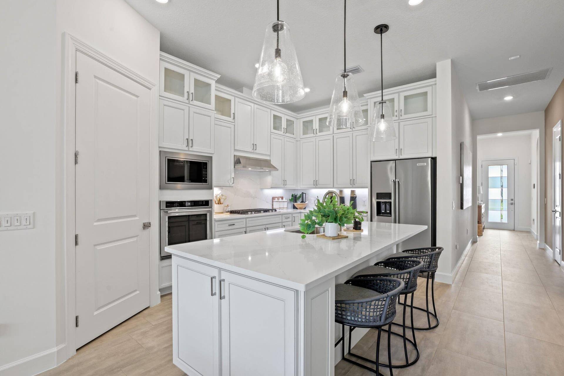 205 GEILLIS Path, Delray Beach, FL 33445 Kitchen featuring white shaker-style cabinetry with glass-front uppers, solid surface countertops, a central island, stainless steel appliances, and glass pendant lighting
