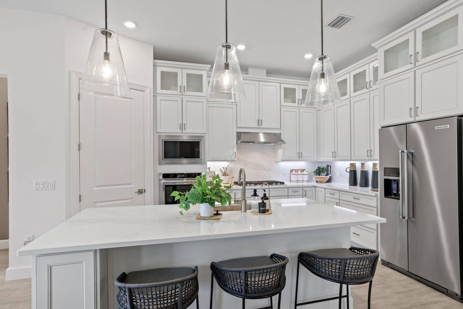 205 GEILLIS Path, Delray Beach, FL 33445 Kitchen featuring white cabinetry with glass-front uppers, solid-surface countertops, a large center island, stainless steel appliances, and three clear glass pendant lights