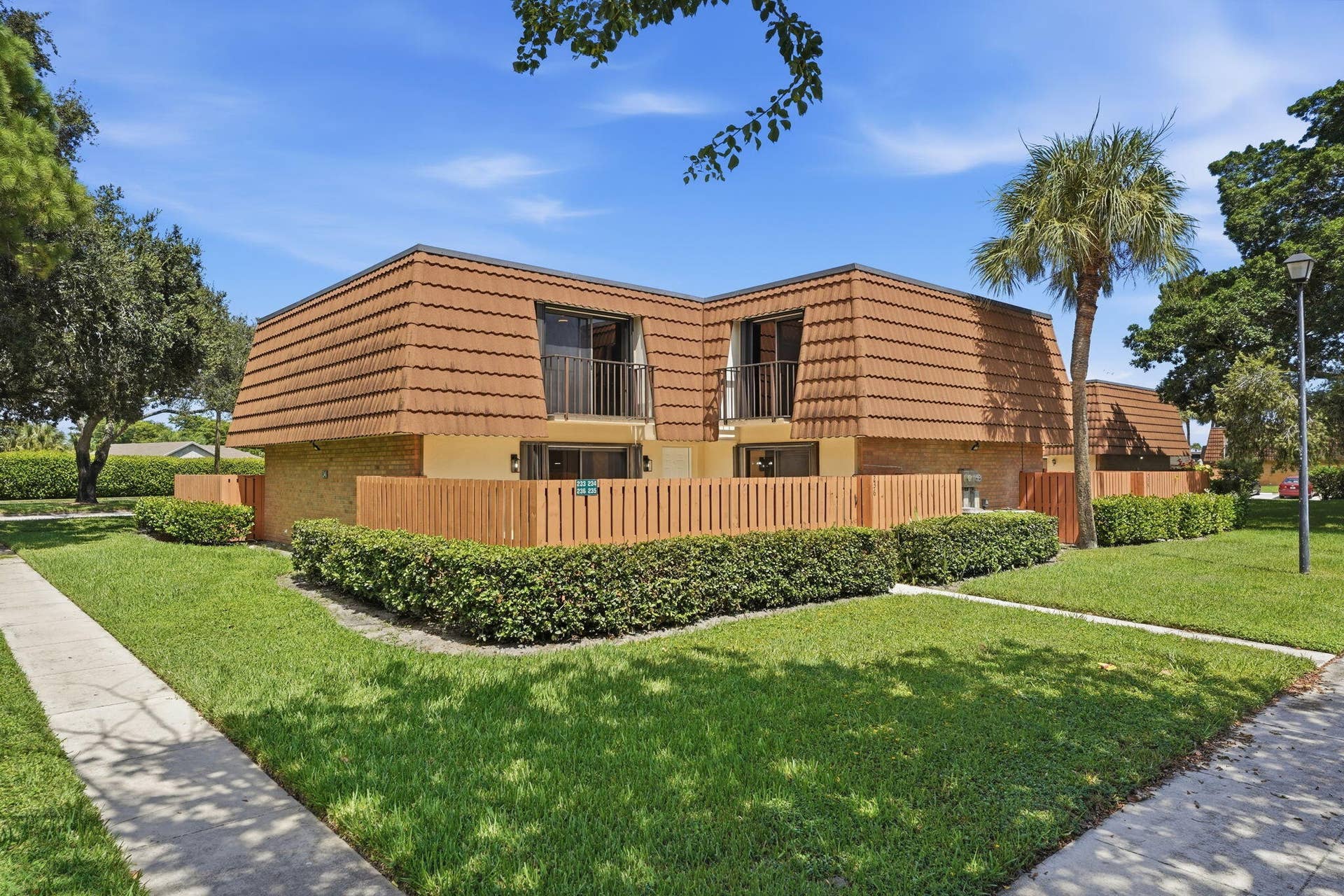 236 CHARTER Way, West Palm Beach, FL 33407 Front exterior featuring a mansard roof, private balconies, a fenced patio area, and mature landscaping