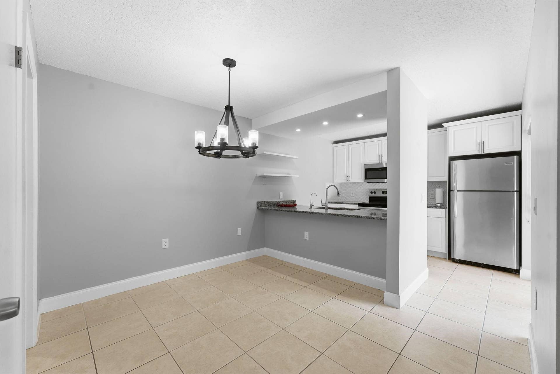 236 CHARTER Way, West Palm Beach, FL 33407 Open concept layout with tile flooring, a contemporary chandelier, kitchen with white cabinetry, stainless steel appliances, and a breakfast bar with stone countertops