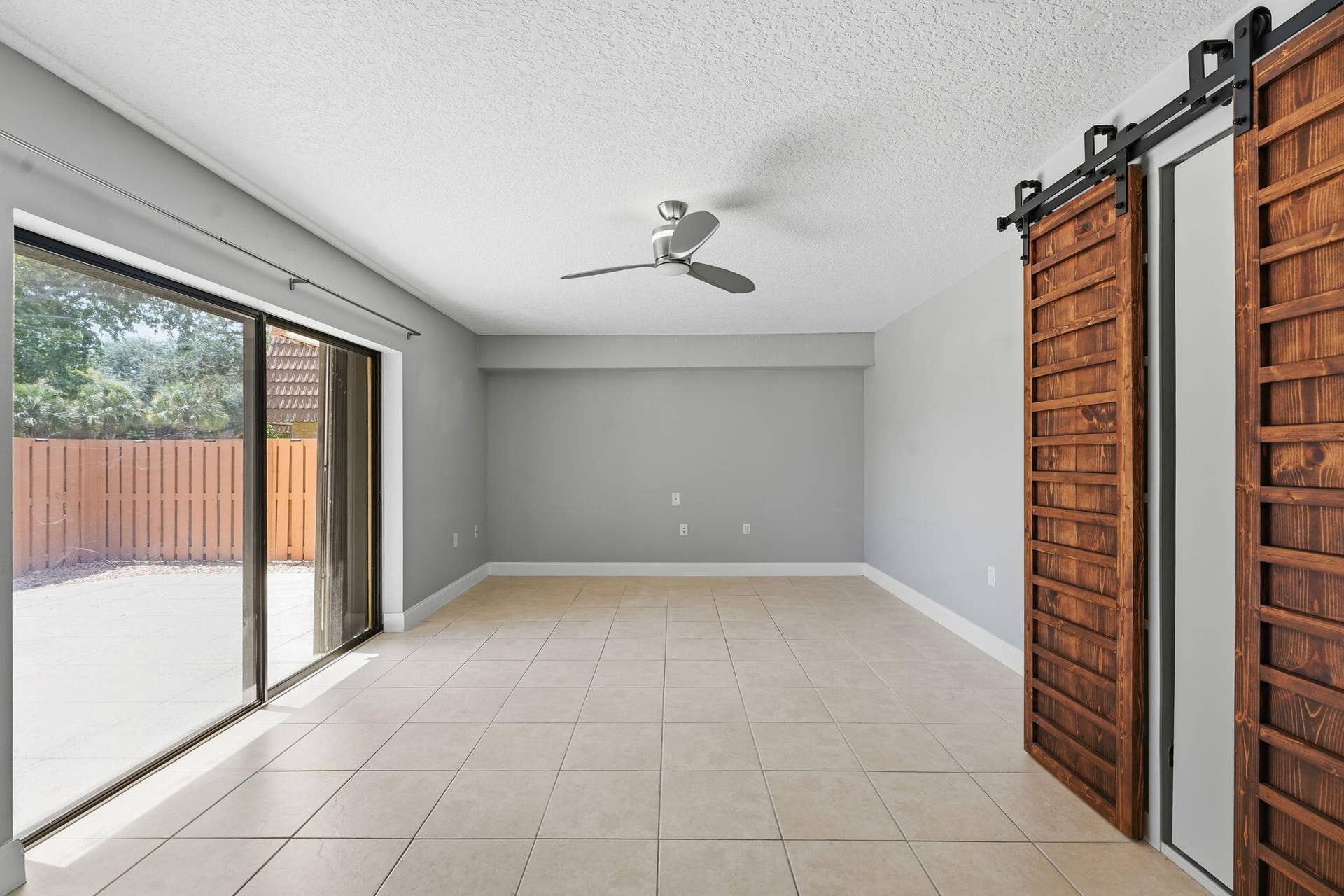 236 CHARTER Way, West Palm Beach, FL 33407 Barn Doors open to a murphy bed. Spacious open room with neutral gray walls, ceiling fan, and tile flooring throughout.