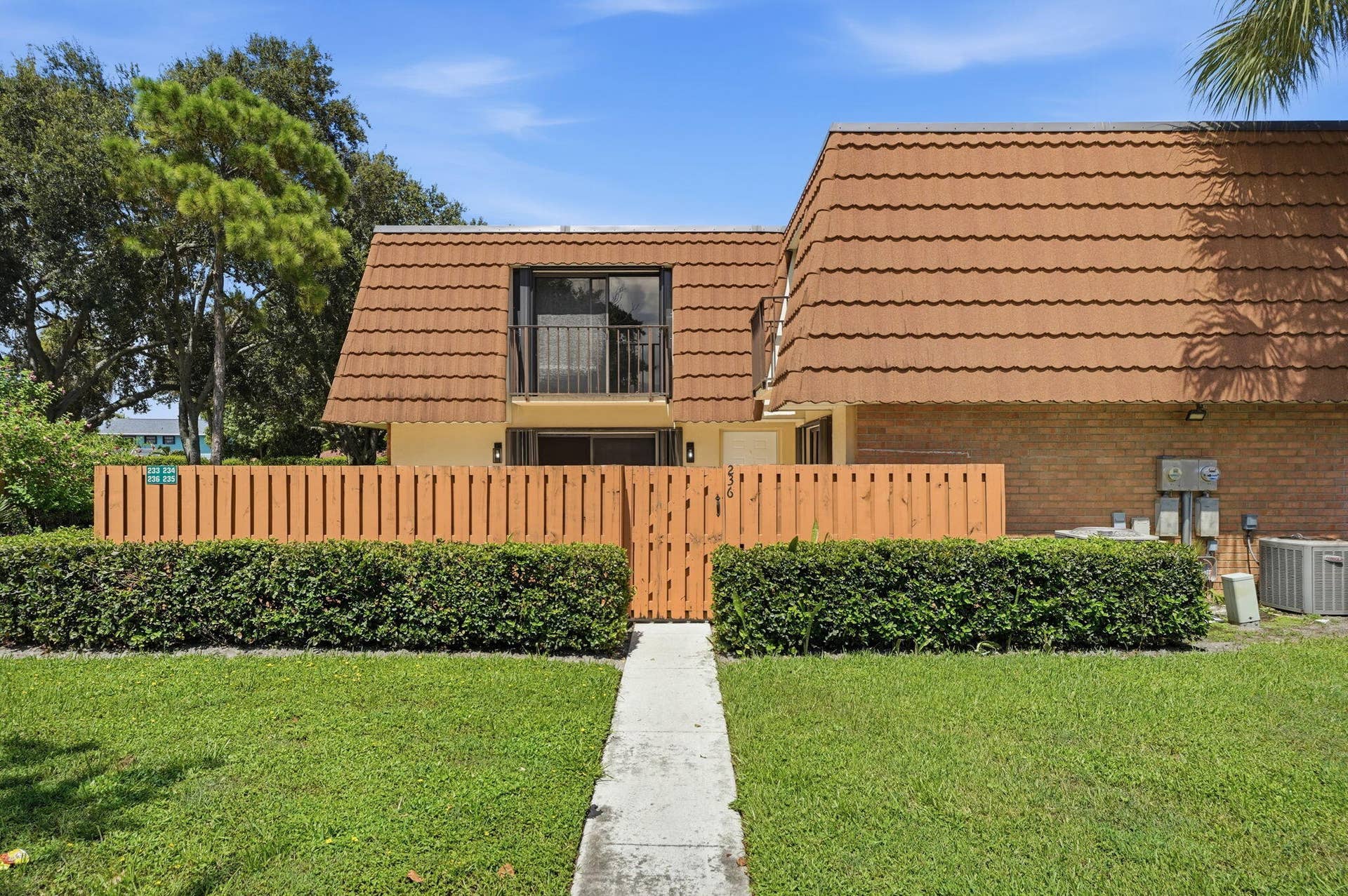236 CHARTER Way, West Palm Beach, FL 33407 Pitched roofline with textured tiles, upper-level balcony with metal railing, privacy fencing, and a manicured lawn