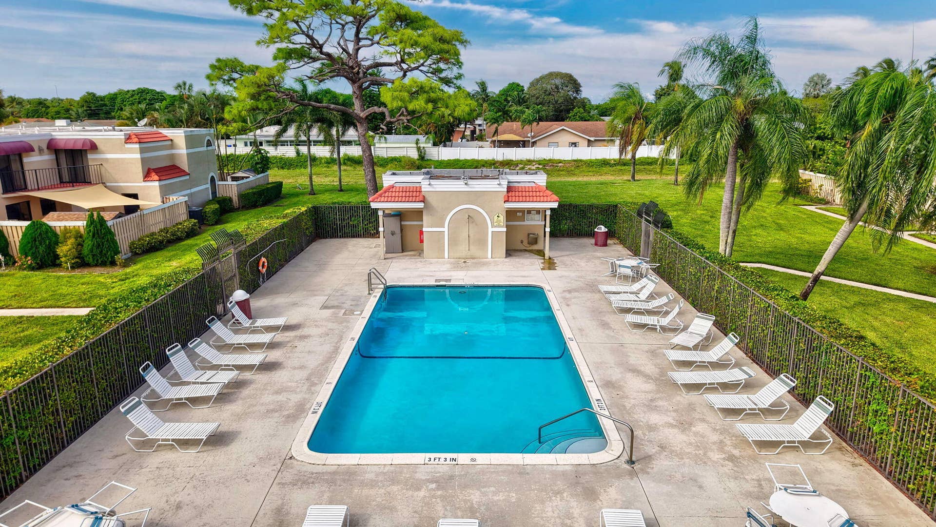 Rectangular swimming pool with a surrounding concrete deck, privacy fencing, and a built-in pool house