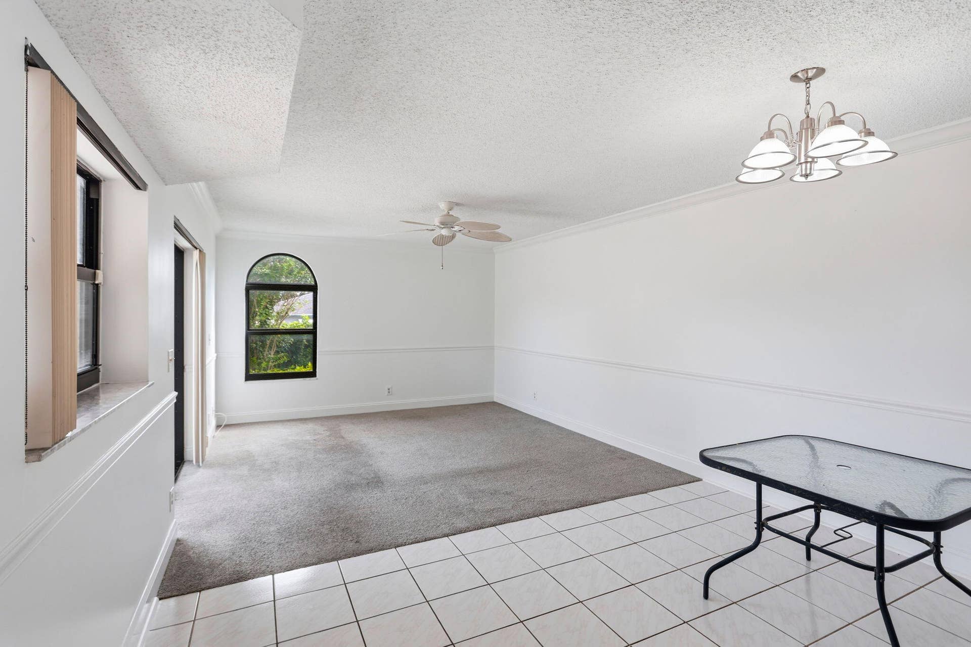 Arched window, ceiling fan, white tile flooring, gray carpeting, and l chandelier
