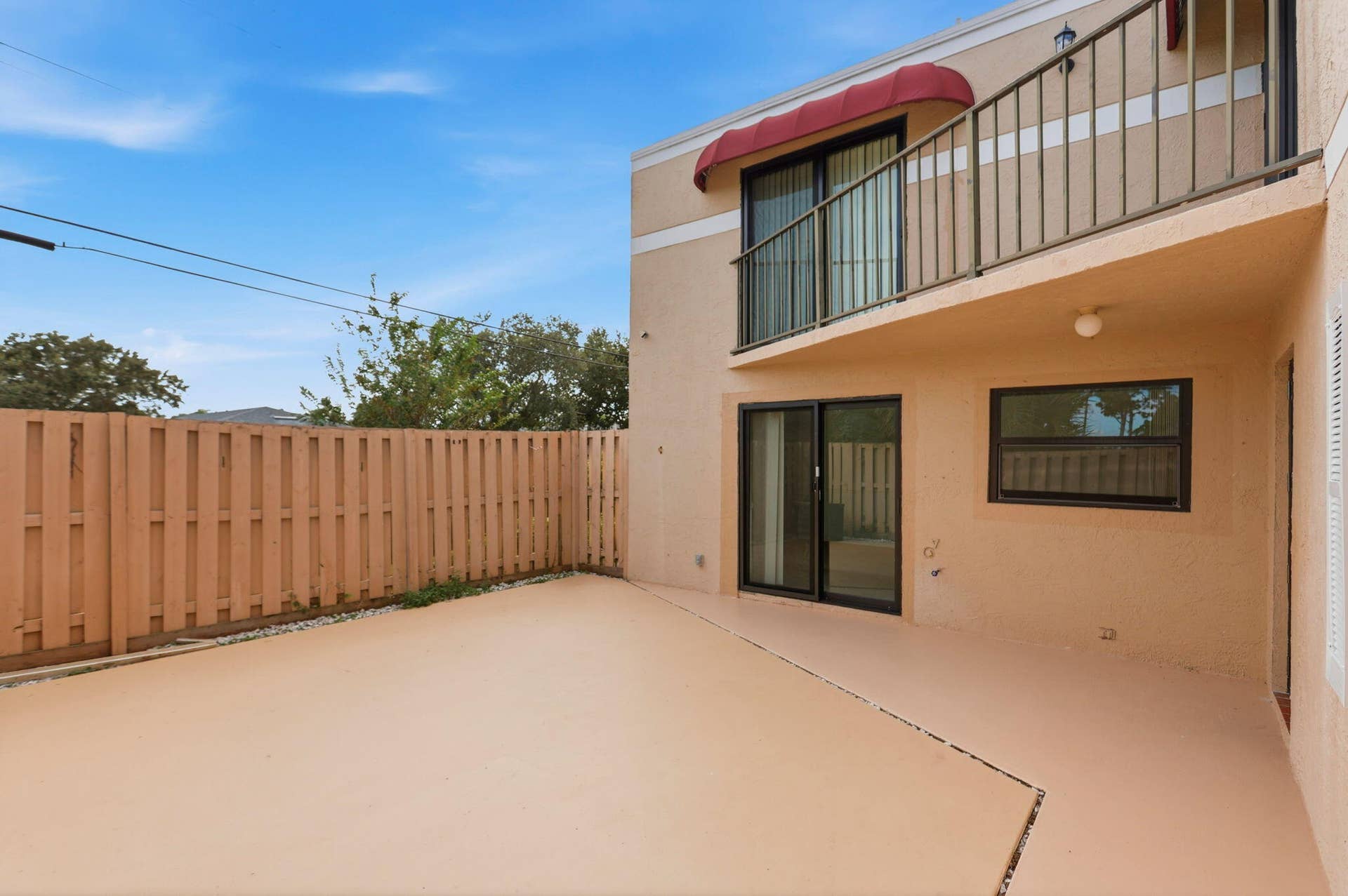 Private patio space featuring a wood-panel fence, upper-level balcony with metal railing, and a red fabric awning