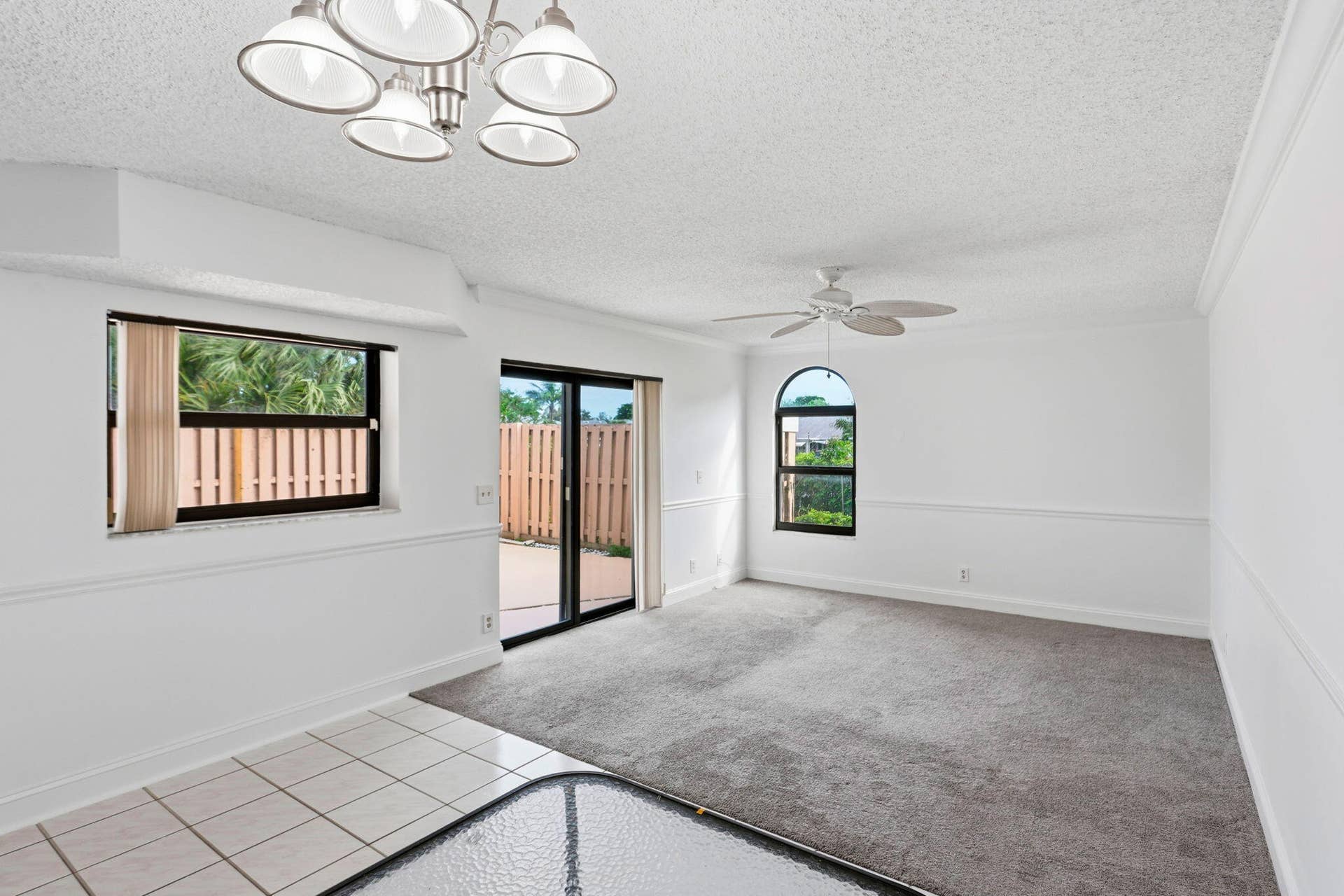 Sliding glass doors to outdoor patio, arched window, ceiling fan, contemporary chandelier, and wainscoting