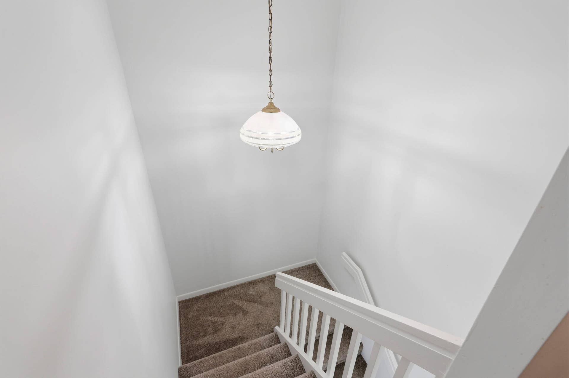 Carpeted staircase with white balusters, a white handrail, and a hanging pendant light fixture