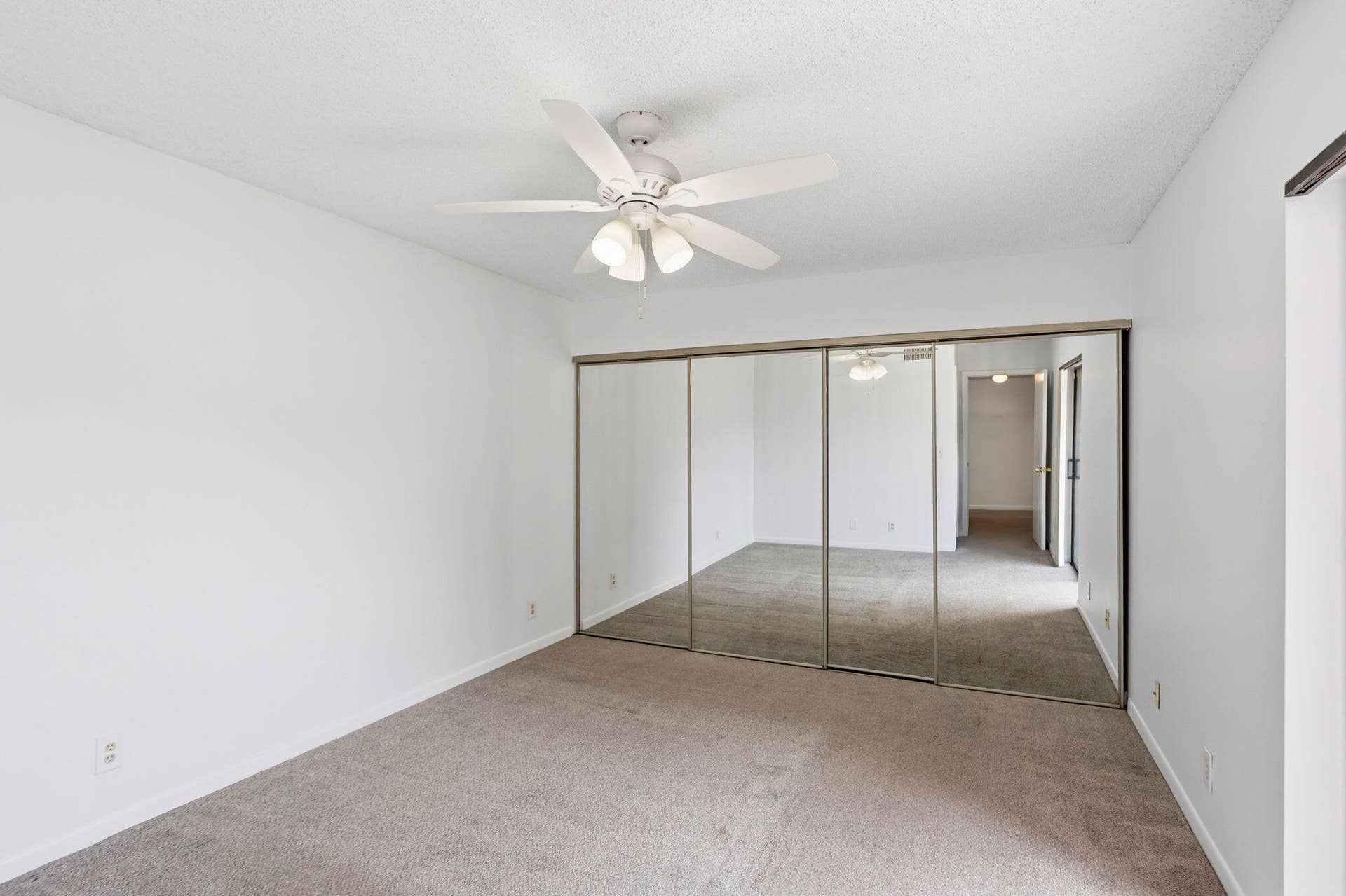 Ceiling fan with integrated lighting, mirrored sliding closet doors, and neutral carpeting