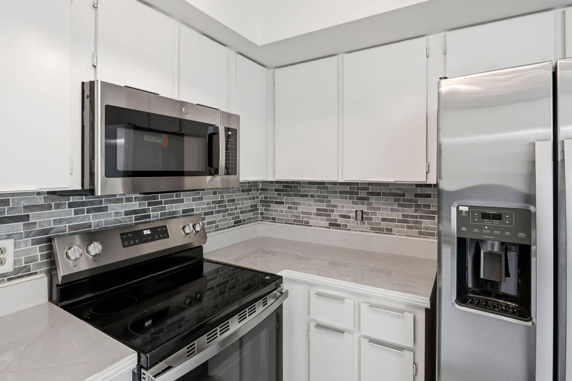 NEW Stainless steel appliances, white cabinetry, tile backsplash, and light-toned countertops