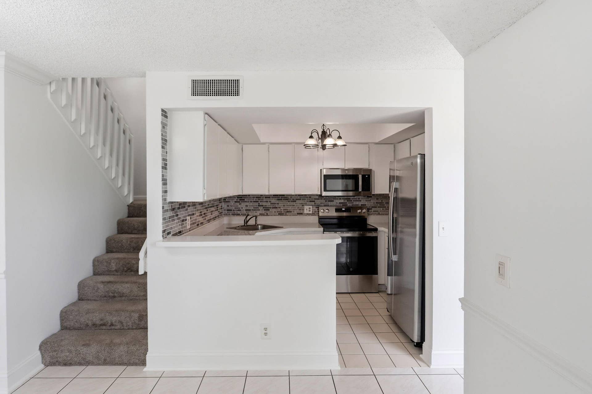 Kitchen with NEWE stainless steel appliances, white cabinetry, and a mosaic tile backsplash