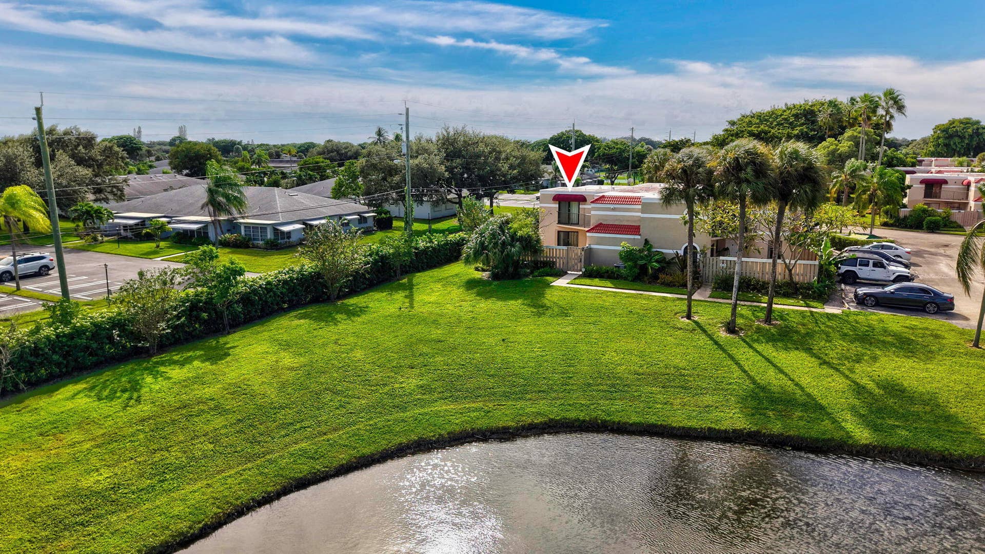 Two-story structure with red awnings, light-toned exterior, mature palm trees, and manicured green space
