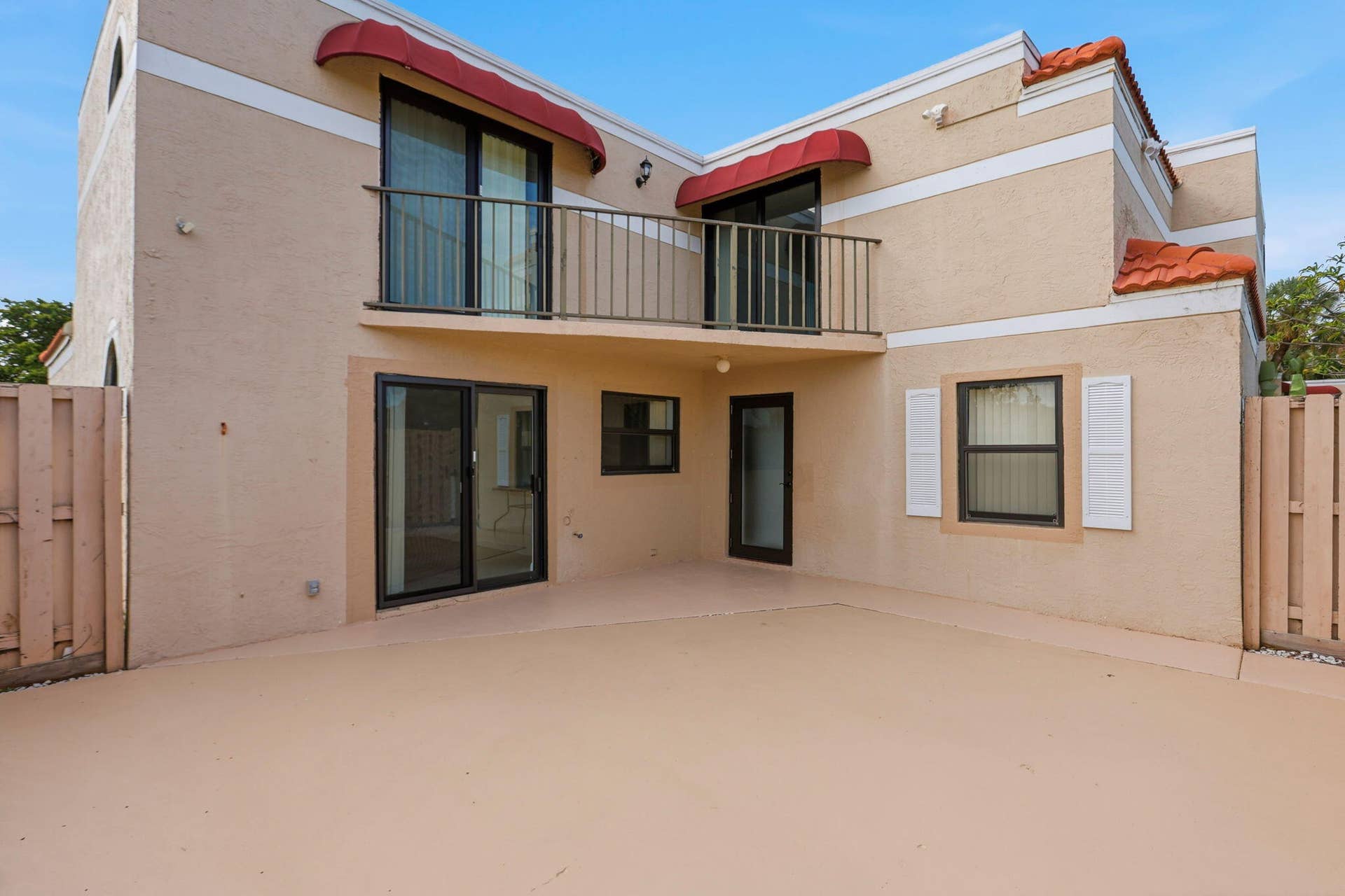 Spacious exterior patio with stucco finish, upper-level balcony with metal railing, multiple sliding glass doors, and window with exterior shutters