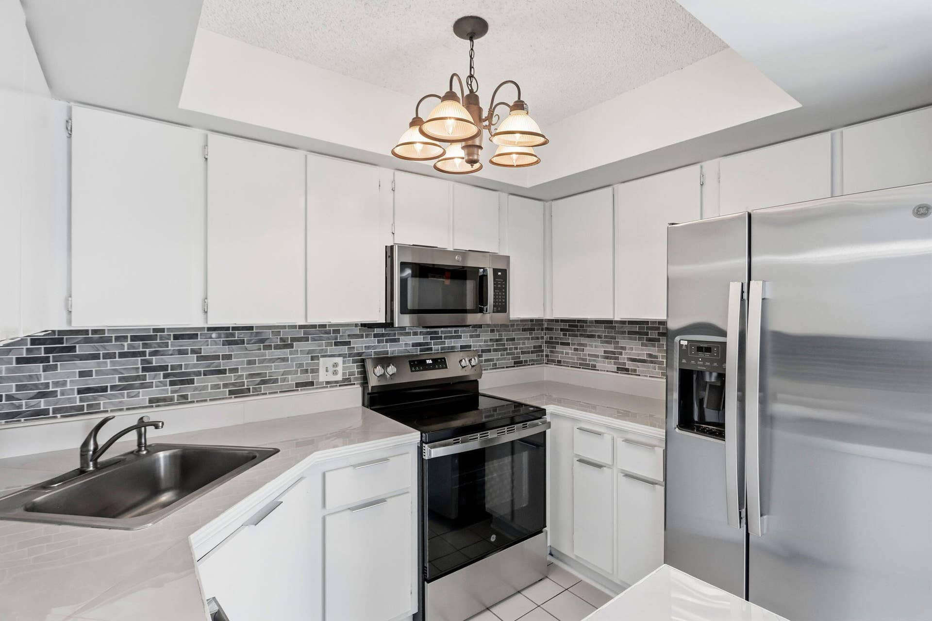 White cabinetry, mosaic tile backsplash, NEW stainless steel appliances, recessed lighting, and a multi-light chandelier