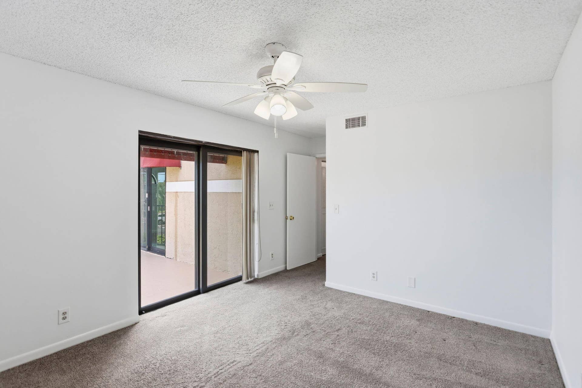 Plush grey carpeting, white ceiling with texture, ceiling fan with integrated lighting, glass sliding doors, and white interior walls