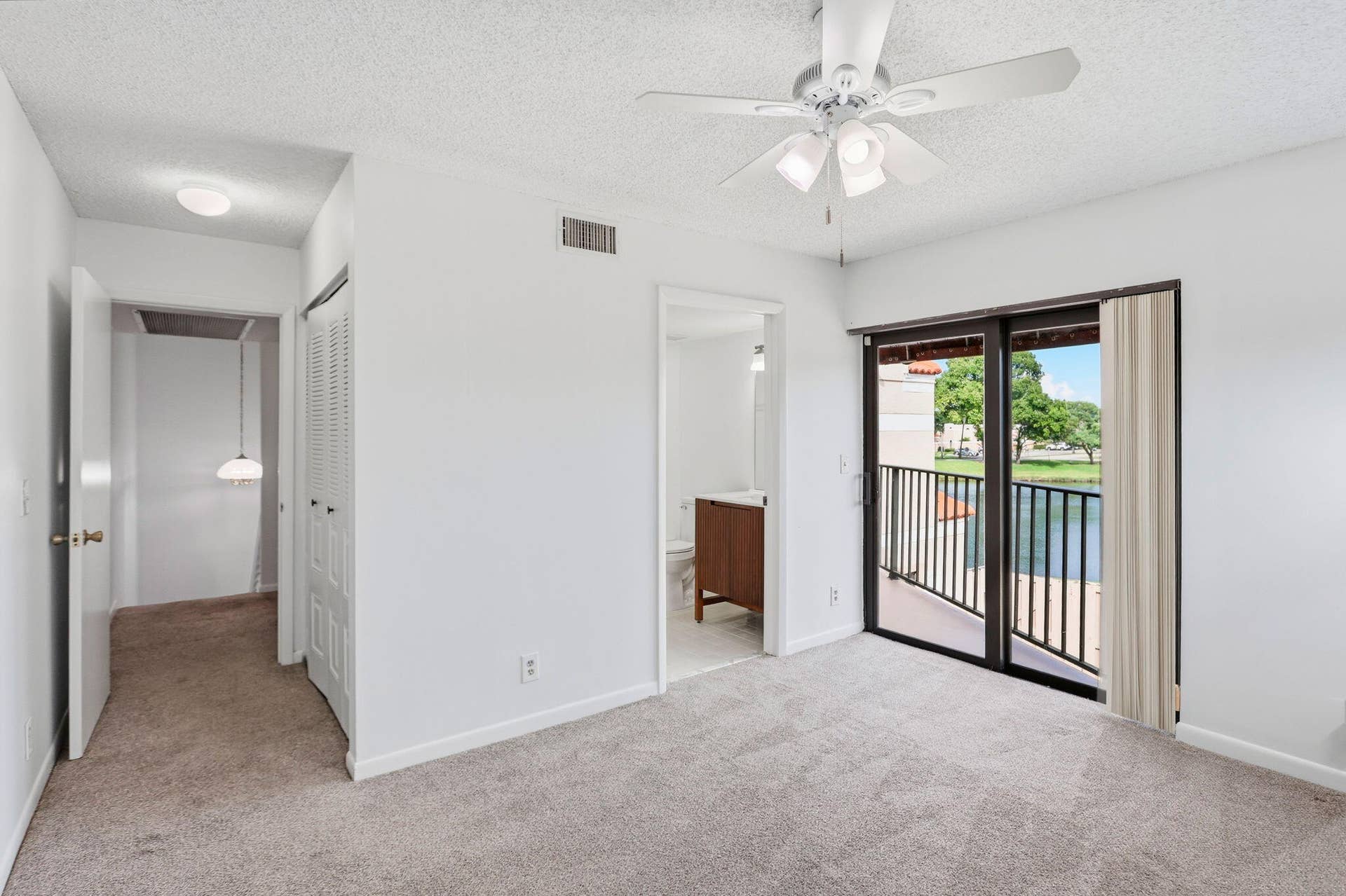 Carpeted room with a ceiling fan, sliding glass doors, and a private balcony overlooking a water feature