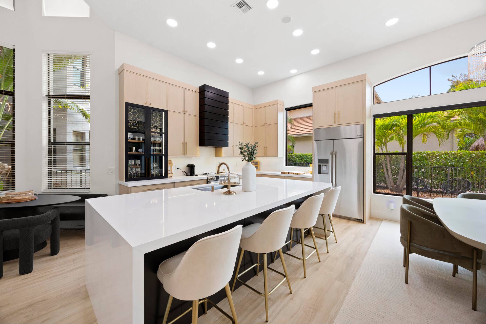 Kitchen featuring light-tone cabinetry, a large waterfall-edge island with solid-surface countertops, stainless steel appliances, and high ceilings with recessed lighting