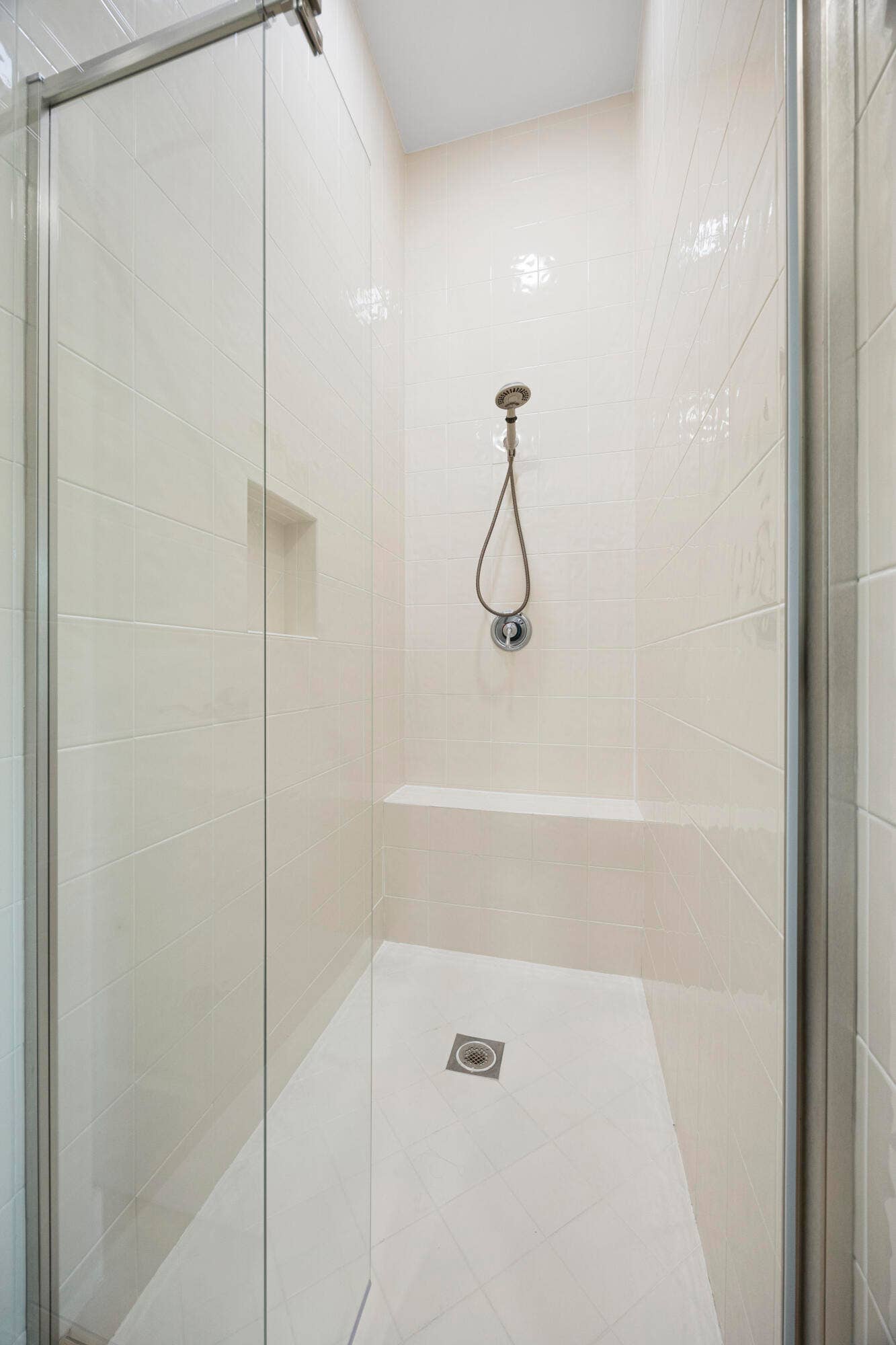 Walk-in shower featuring floor-to-ceiling tile, a frameless glass door, a built-in bench, an integrated wall niche, and a handheld shower fixture