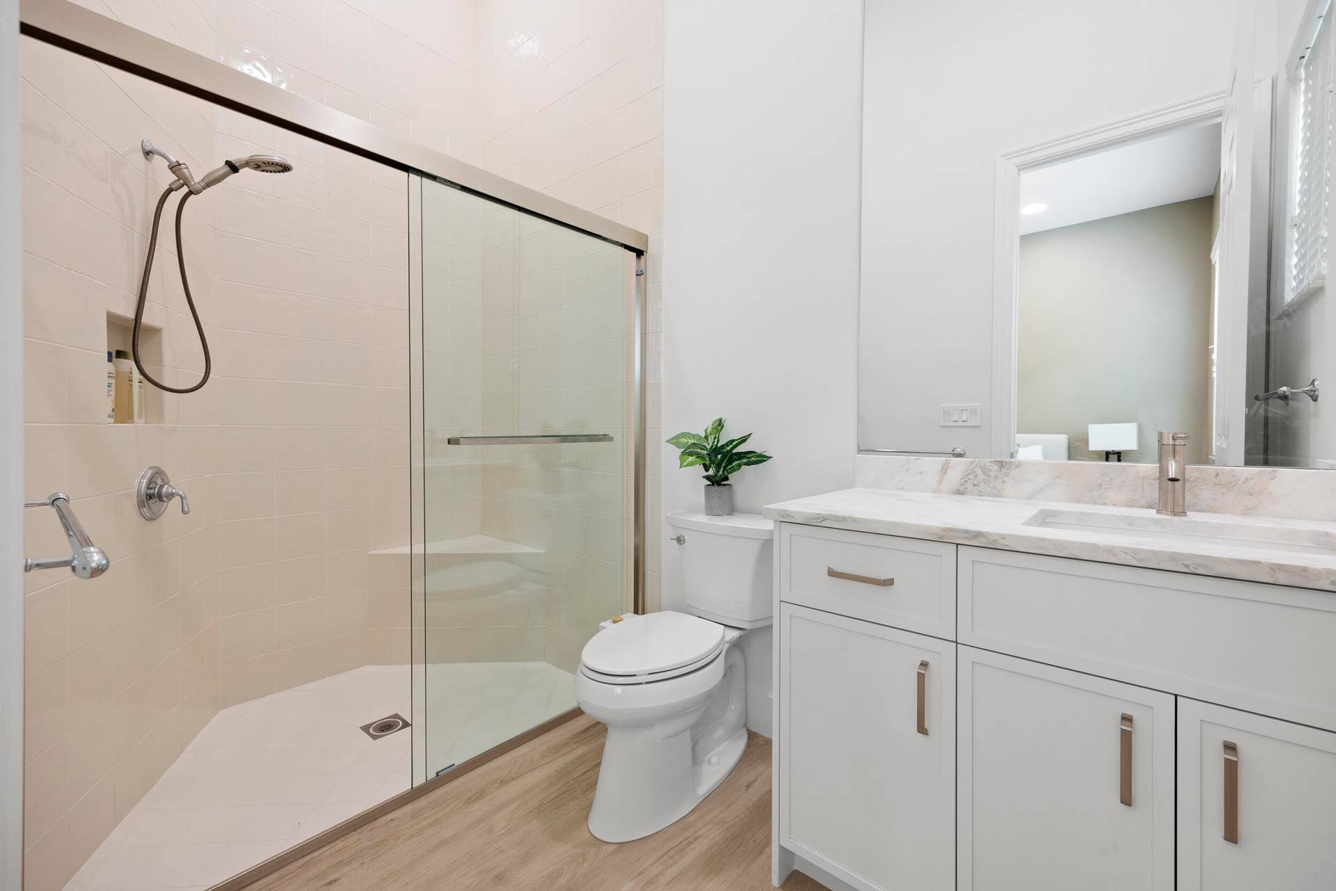Bathroom featuring a walk-in shower with a glass enclosure, built-in wall niche, and handheld showerhead, complemented by a white vanity with a stone countertop and metal hardware