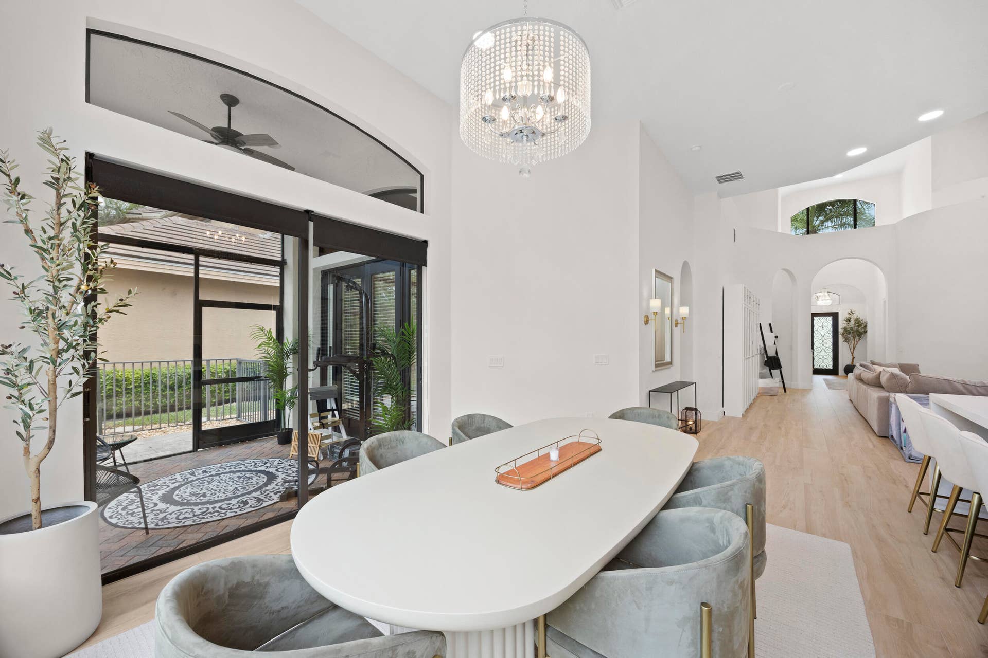 High-ceilinged interior featuring a tiered crystal chandelier, wood-finish flooring, arched architectural details, and a multi-panel glass sliding door system