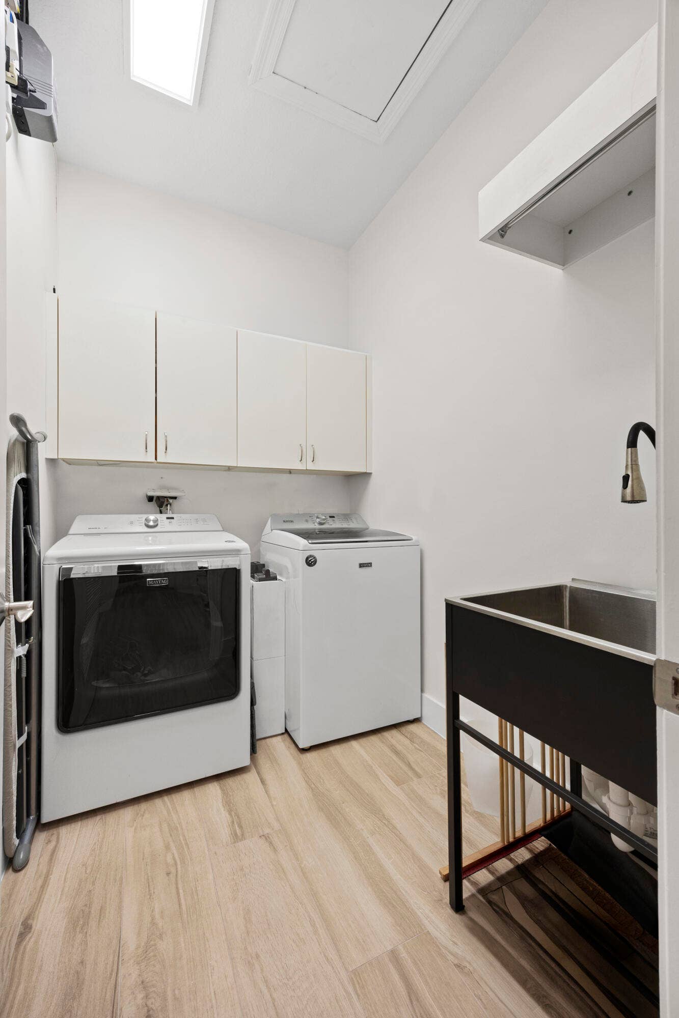 Laundry space featuring white upper cabinetry, wood-finish flooring, a utility sink with a high-arch pull-down faucet, and overhead lighting