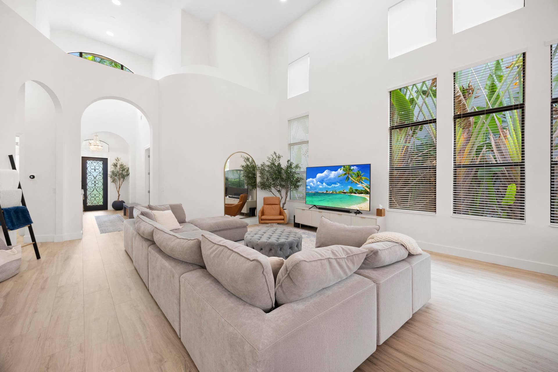 High-ceiling living area featuring arched architectural details, wood-finish flooring, and expansive windows with custom blinds