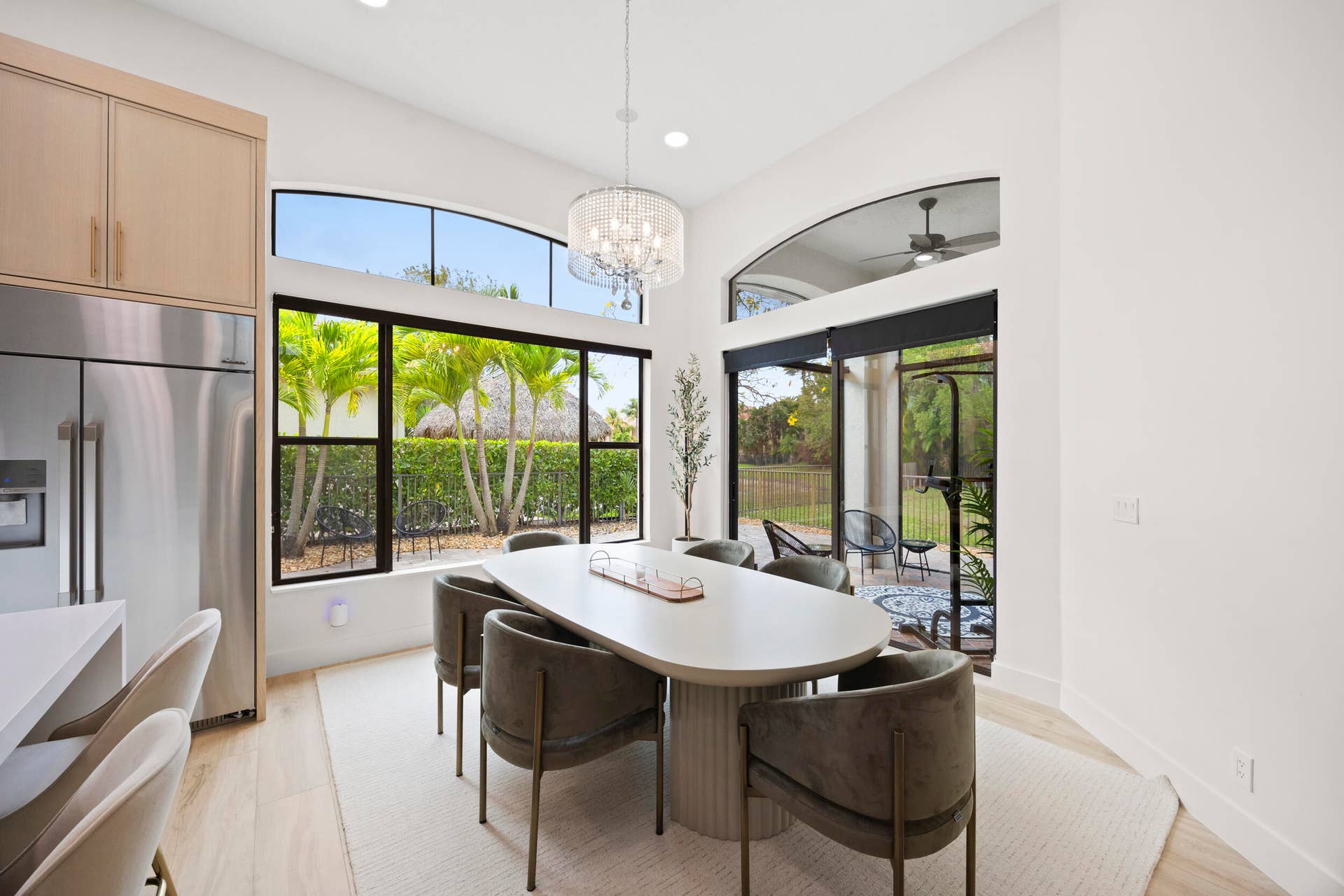 Dining area featuring vaulted ceilings, floor-to-ceiling windows with transoms, modern tiered crystal chandelier, and sliding glass doors