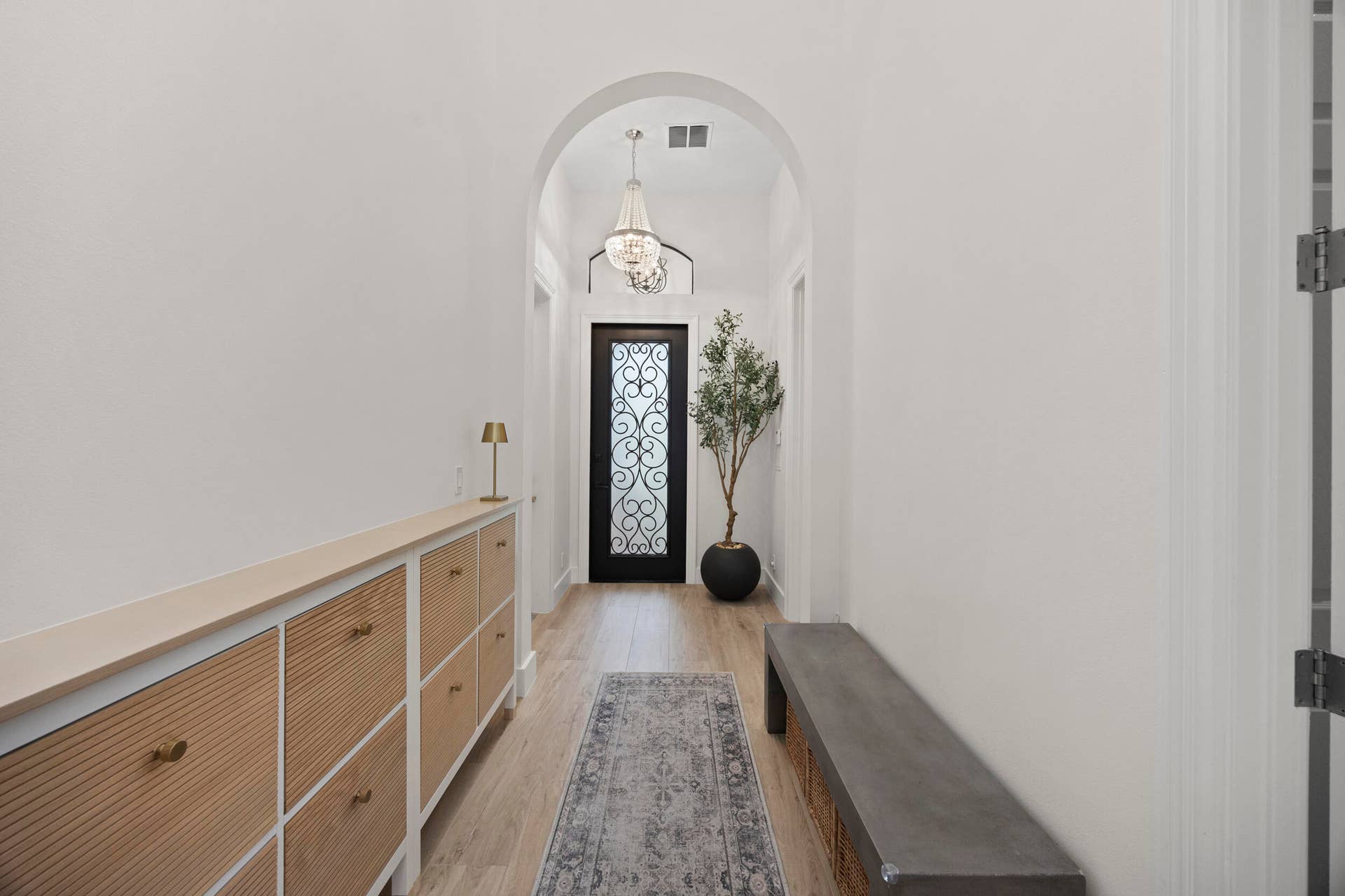 Entryway featuring an arched ceiling, custom built-in cabinetry with textured paneling, wood-finish flooring, and a decorative metal and glass front door accented by an overhead chandelier