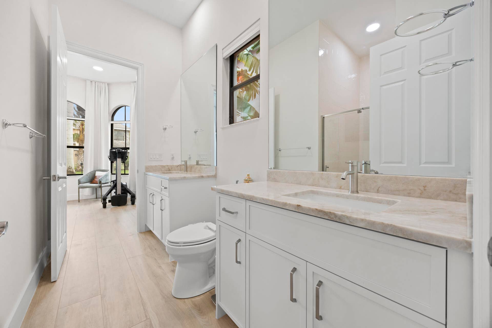 Dual-sink vanity with stone countertops and undermount basins, complemented by white cabinetry, full-height wall mirrors, and wood-finish flooring