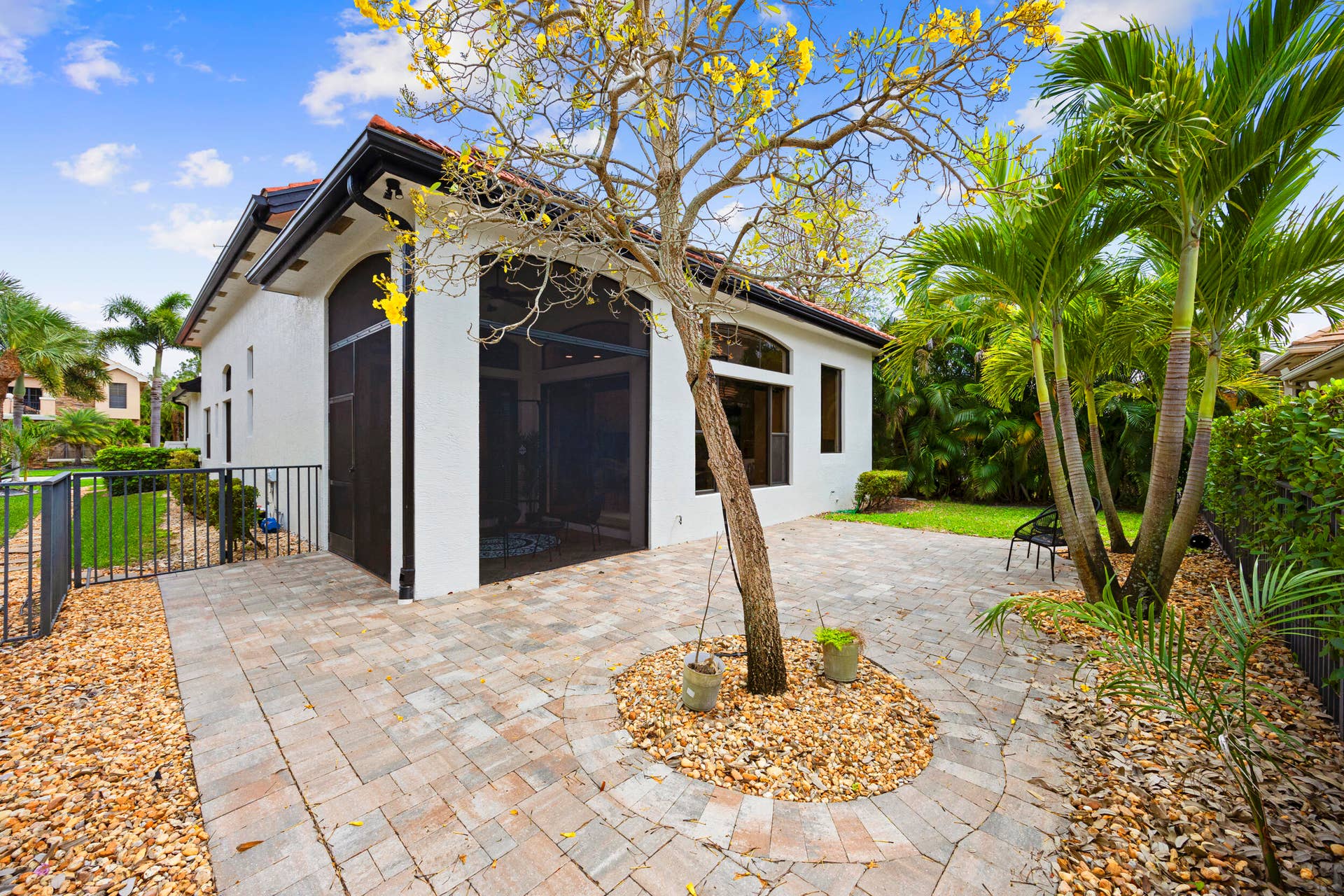 Paved stone patio featuring a screened-in lanai, decorative gravel landscaping, and mature palm trees