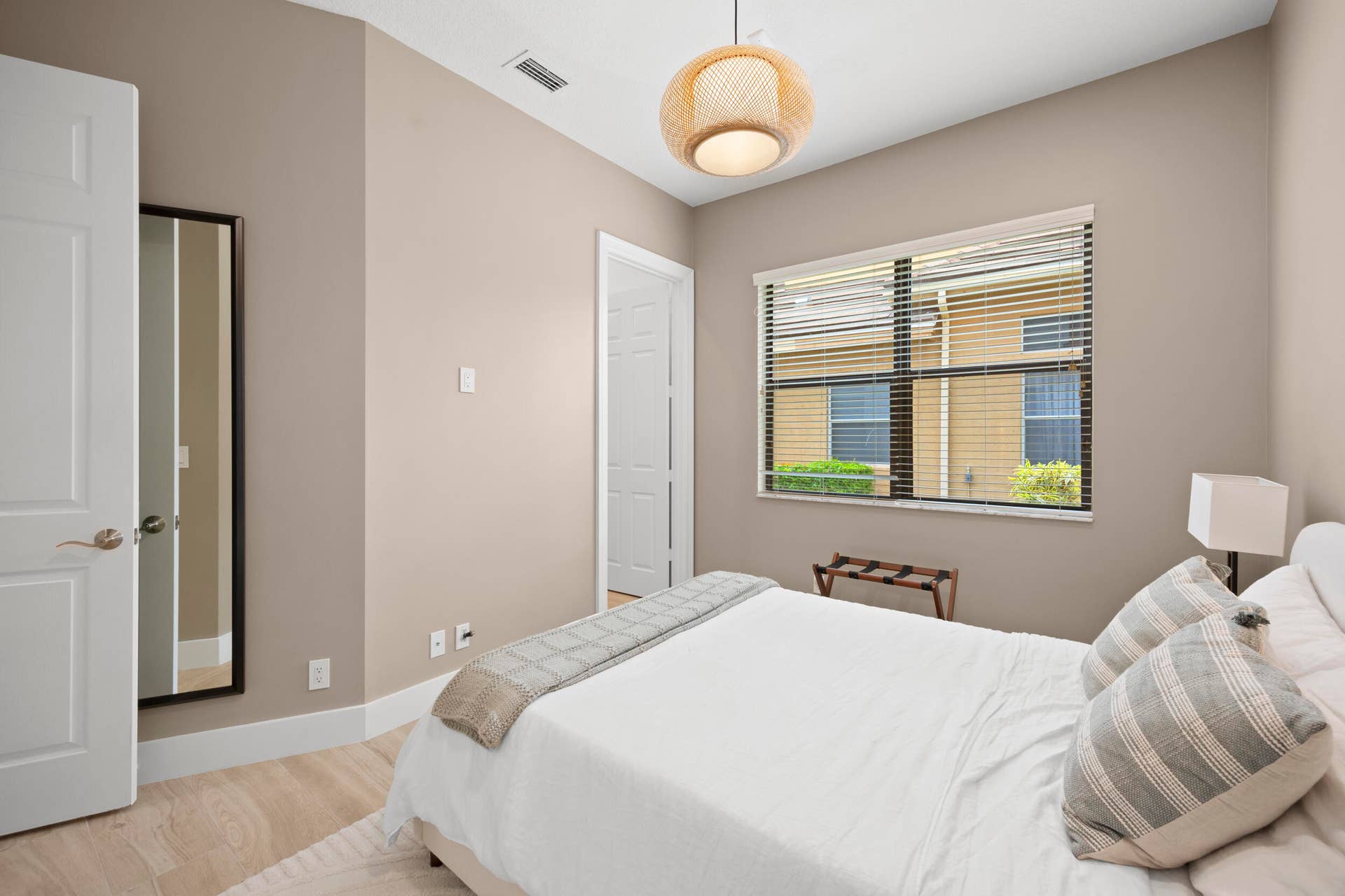 Neutral interior room featuring light wood-finish flooring, a woven pendant light fixture, and a window with integrated blinds