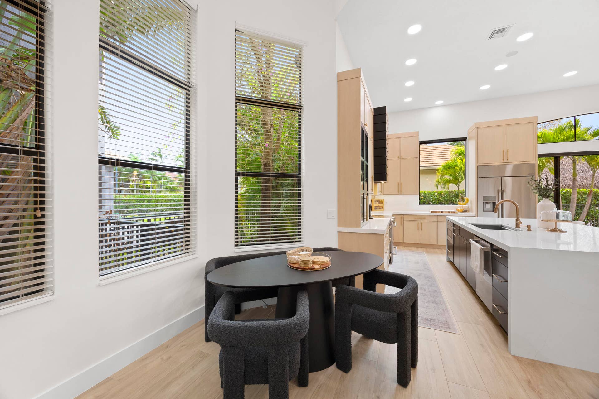 Kitchen featuring light wood-finish cabinetry, a large waterfall-edge island with solid surface countertop, stainless steel refrigerator, recessed lighting, and expansive floor-to-ceiling windows