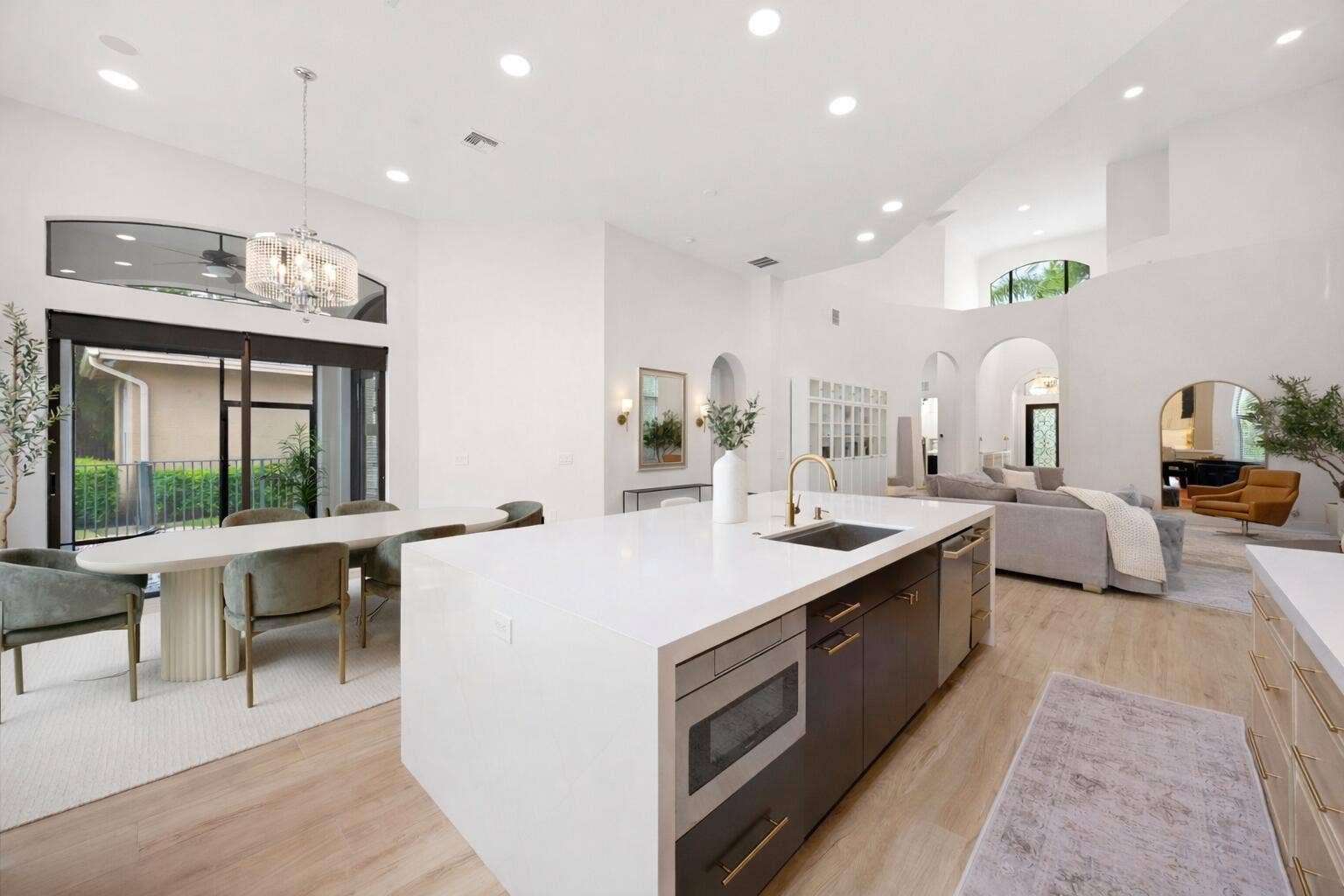 Open-concept kitchen featuring an expansive central island with quartz countertops, custom cabinetry with gold-tone hardware, recessed lighting, and wood-finish flooring