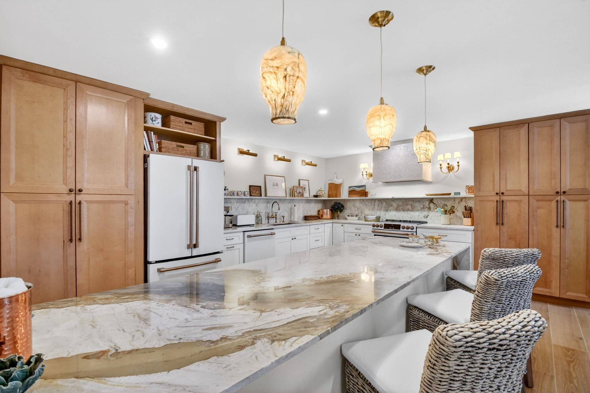 Kitchen featuring full-height wood cabinetry, a waterfall-edge stone island, built-in stainless steel appliances, open shelving, and custom pendant lighting