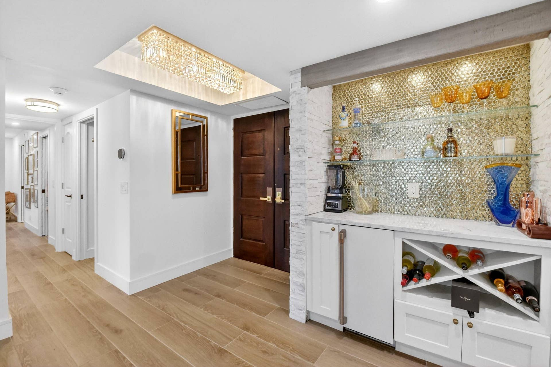 Custom built-in bar featuring white cabinetry, stone-texture backsplash, glass shelving, and integrated wine storage, complemented by wood-finish flooring, recessed crystal lighting, and solid wood double doors