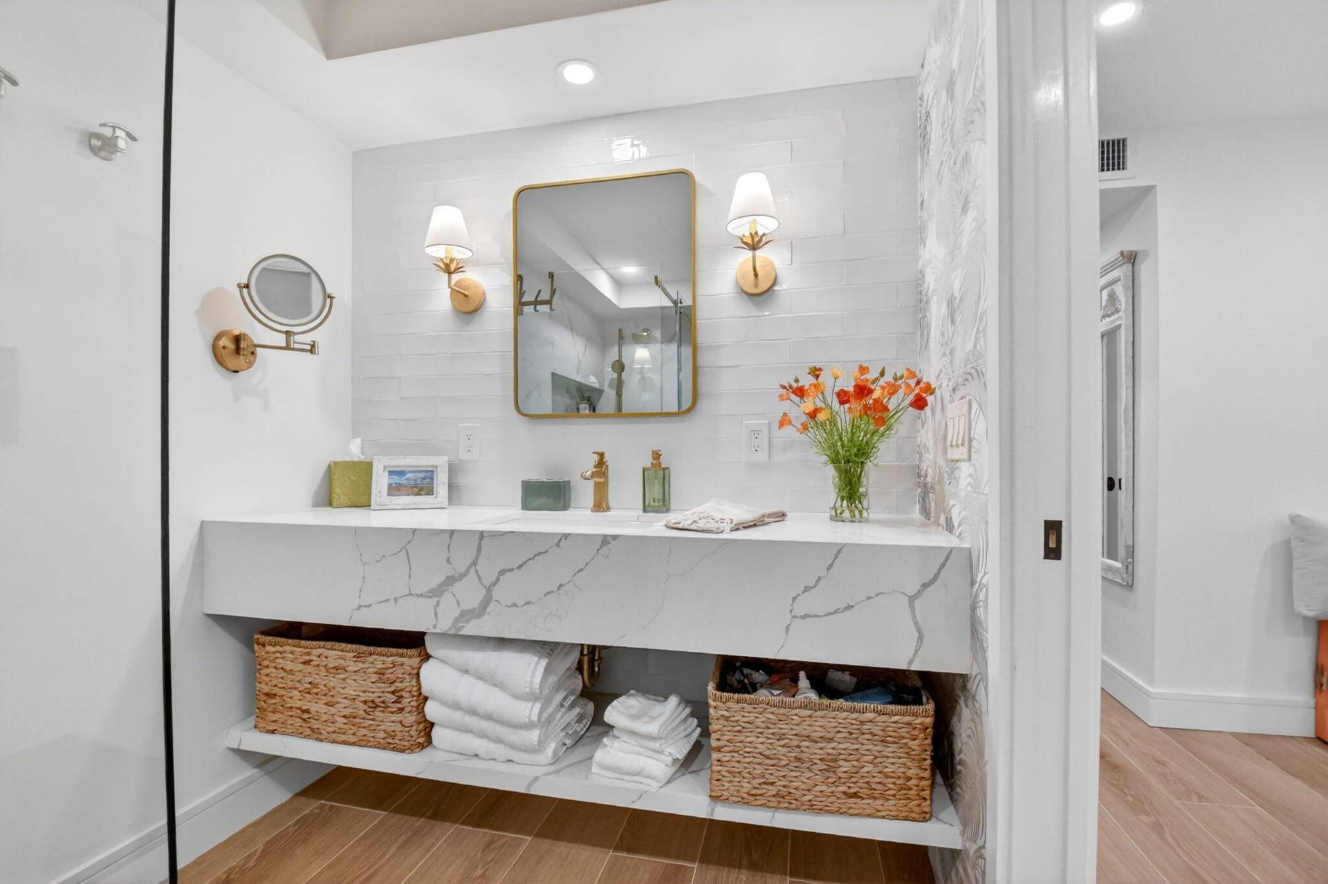Floating vanity featuring a stone-surface countertop with integrated basin, gold-finish faucet, dual wall-mounted light fixtures, and a framed mirror