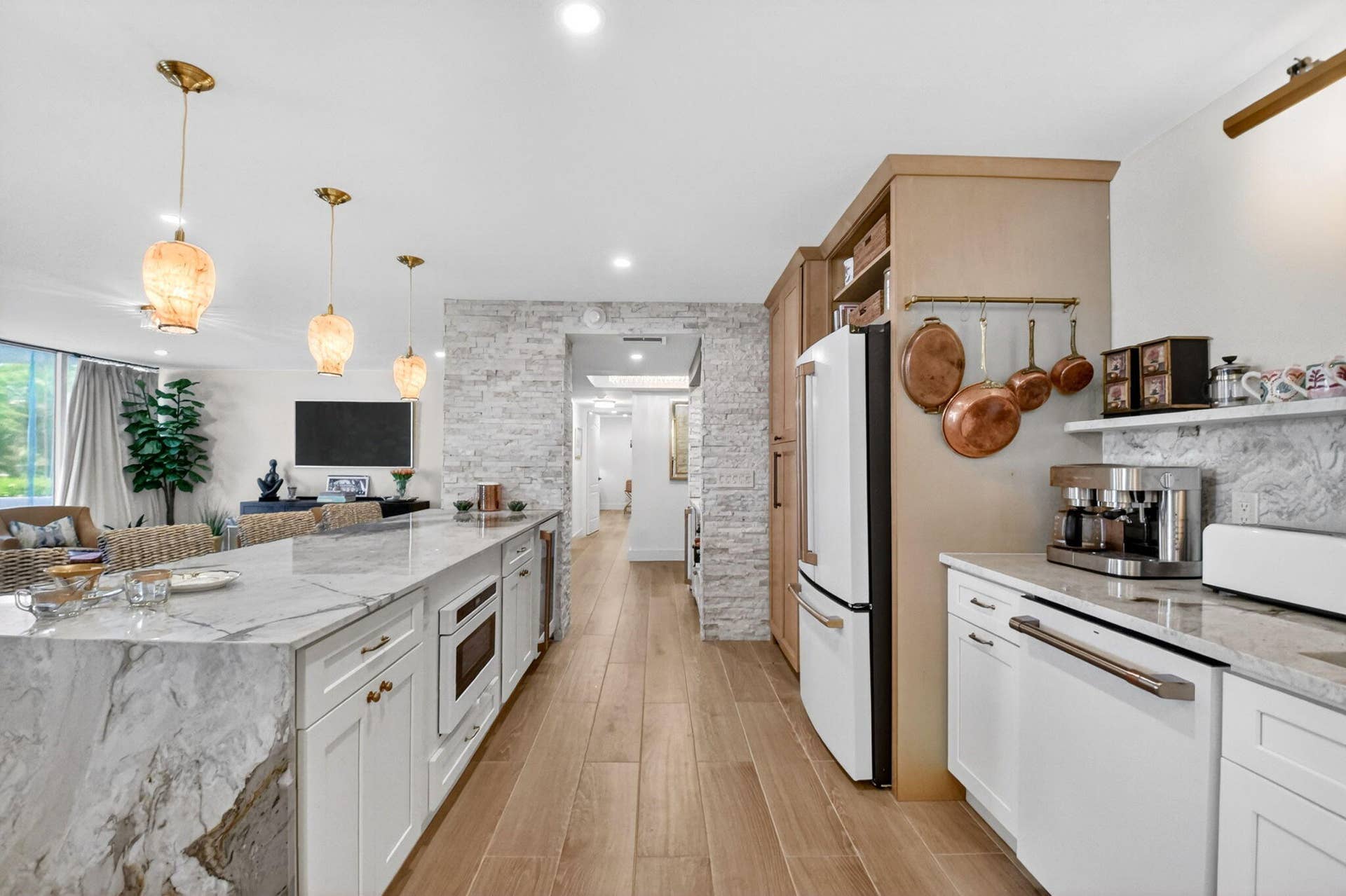 Kitchen featuring a stone-topped waterfall island, custom cabinetry, wood-finish flooring, textured stone accent wall, and three pendant light fixtures