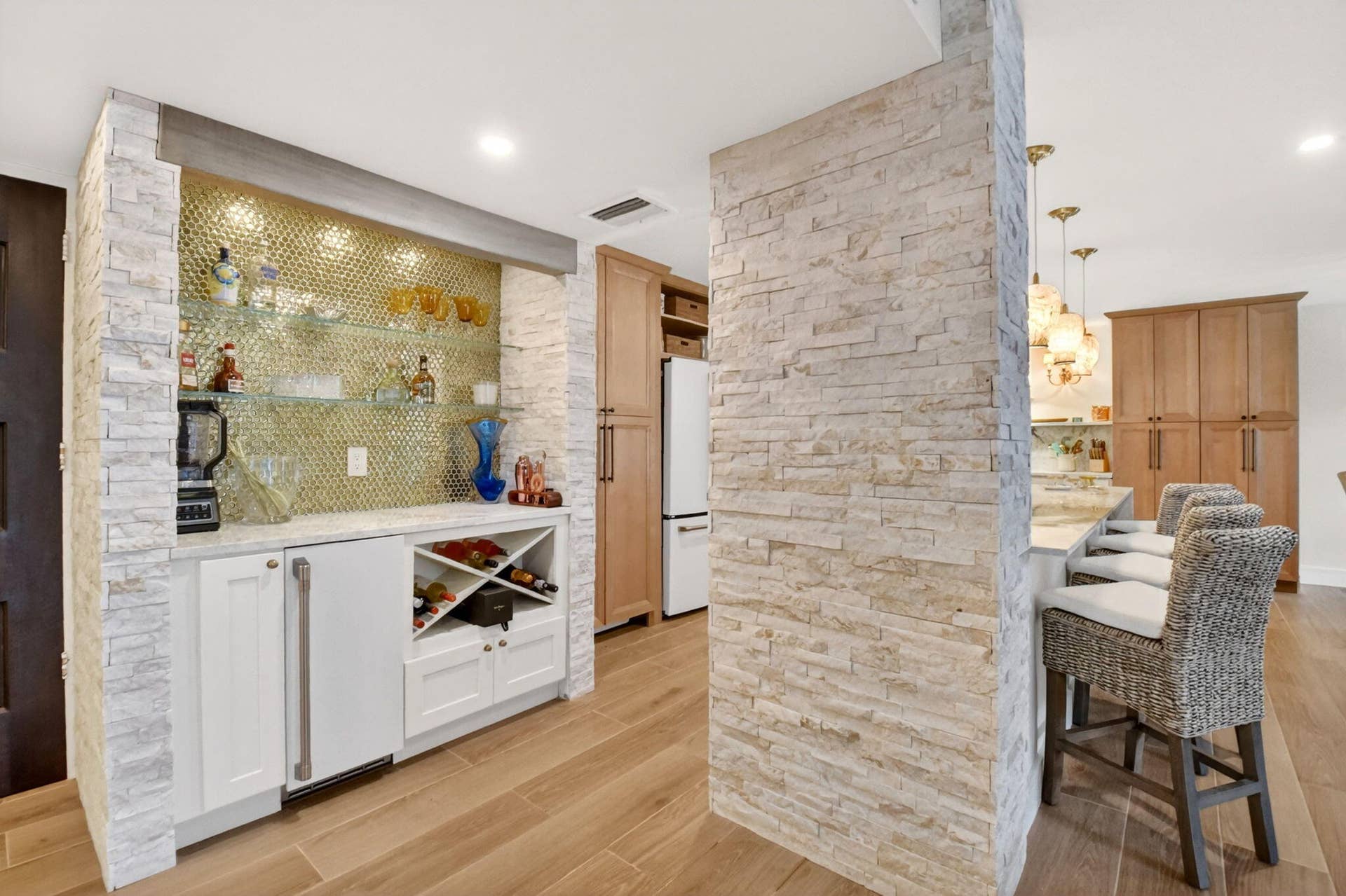 Built-in wet bar featuring stone veneer detailing, glass shelving, metallic tile backsplash, custom cabinetry with wine storage, and wood-finish flooring