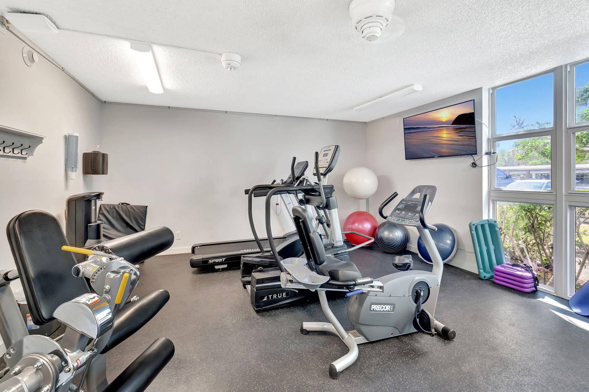 Fitness center featuring durable rubberized flooring, expansive floor-to-ceiling windows, and wall-mounted television
