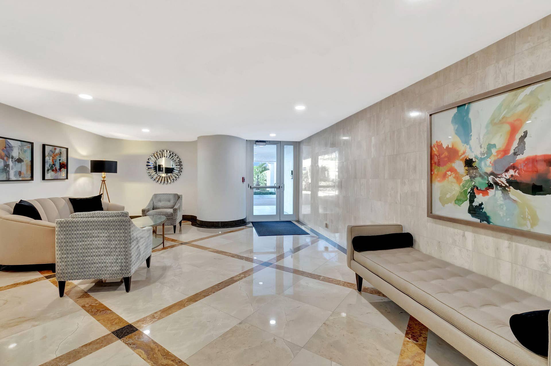 Lobby area featuring polished natural stone flooring with inlaid geometric detailing, floor-to-ceiling stone wall cladding, recessed ceiling lighting, and a glass-paneled entrance door