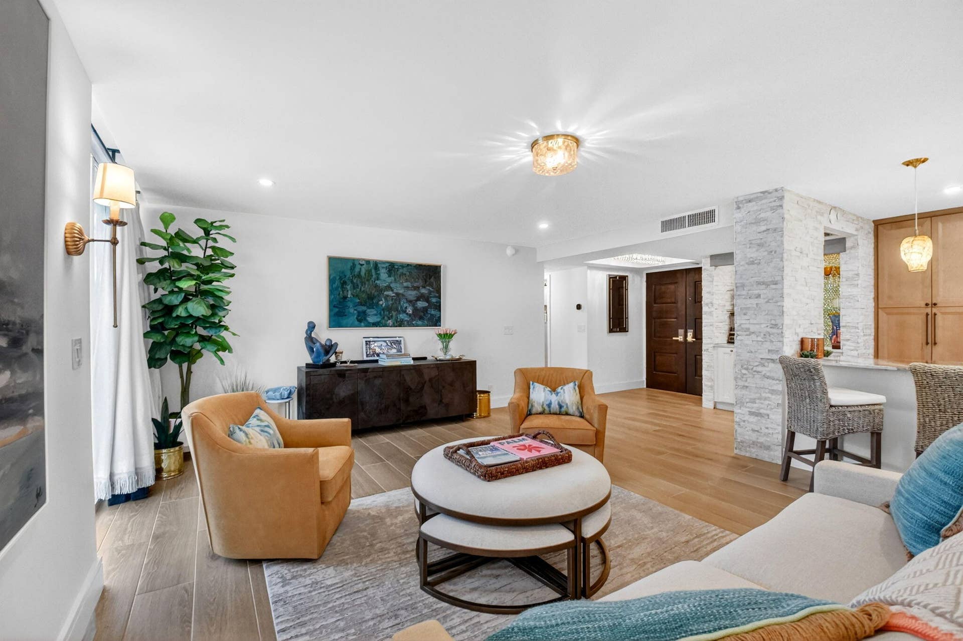 Open-concept interior featuring light wood-finish flooring, a stacked stone accent pillar, recessed ceiling lighting, and a multi-paneled dark wood entry door
