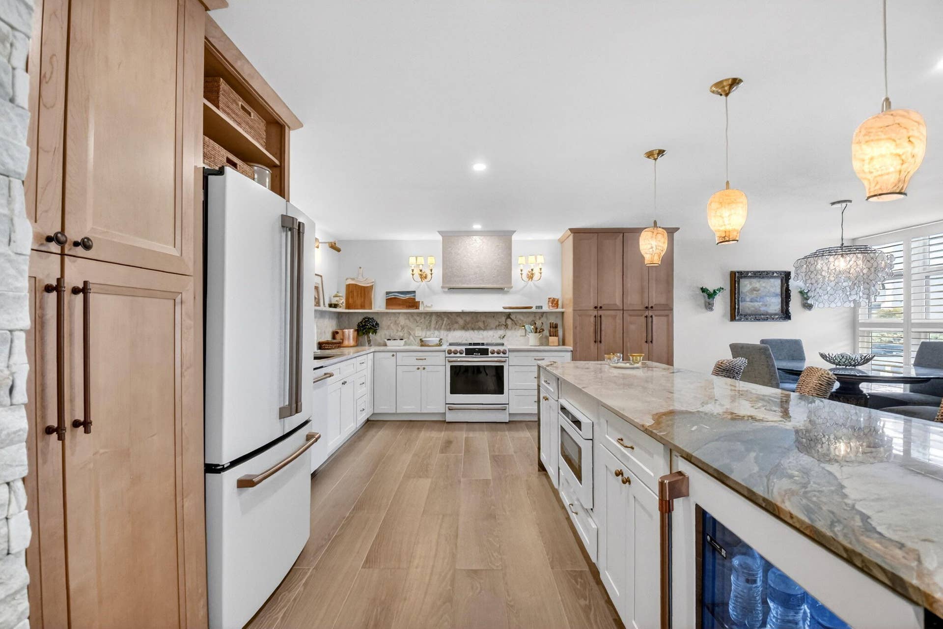 Kitchen featuring wood-finish flooring, white cabinetry with bronze hardware, a stone-surfaced island with an under-counter beverage chiller, and designer pendant lighting