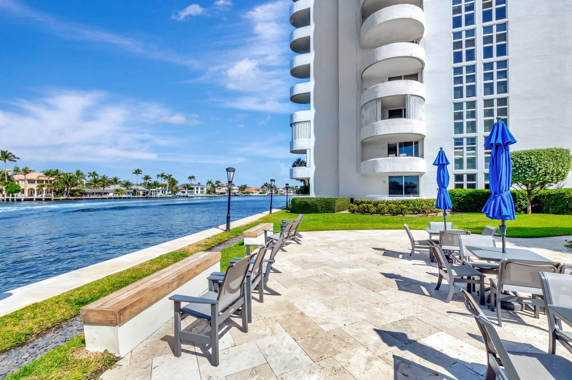 Waterfront stone patio featuring a concrete retaining wall, wood-capped bench seating, and manicured green space